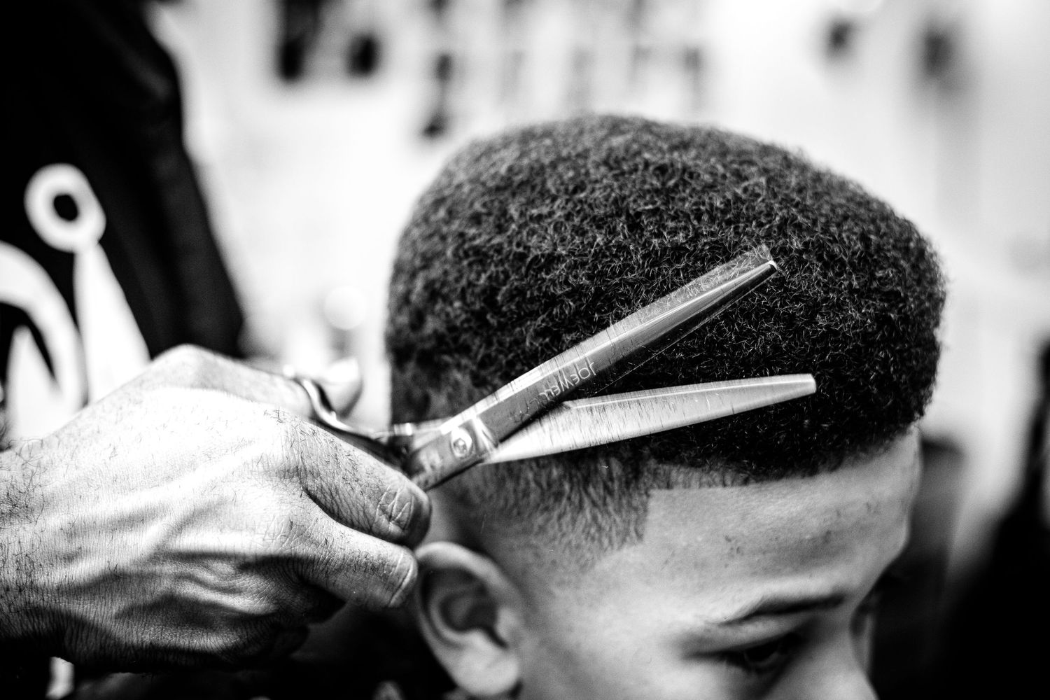 Black and white close-up of scissors and a comb cutting a young boy's short curly hair.