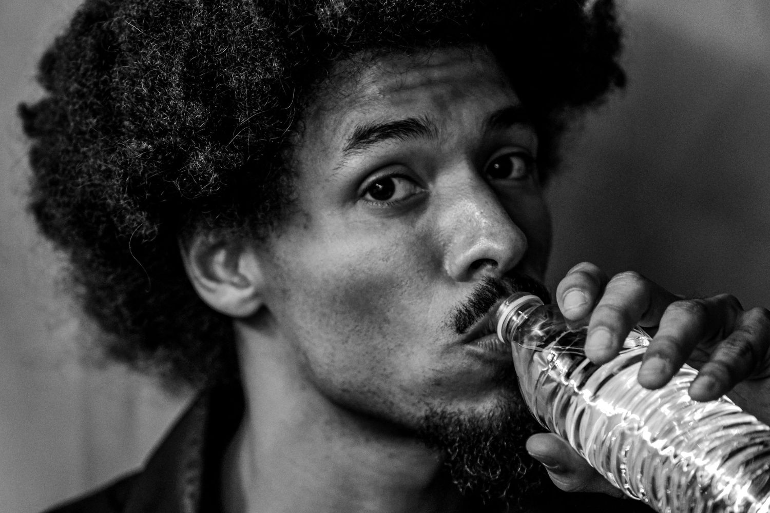 Black and white close-up of man drinking from plastic water bottle.