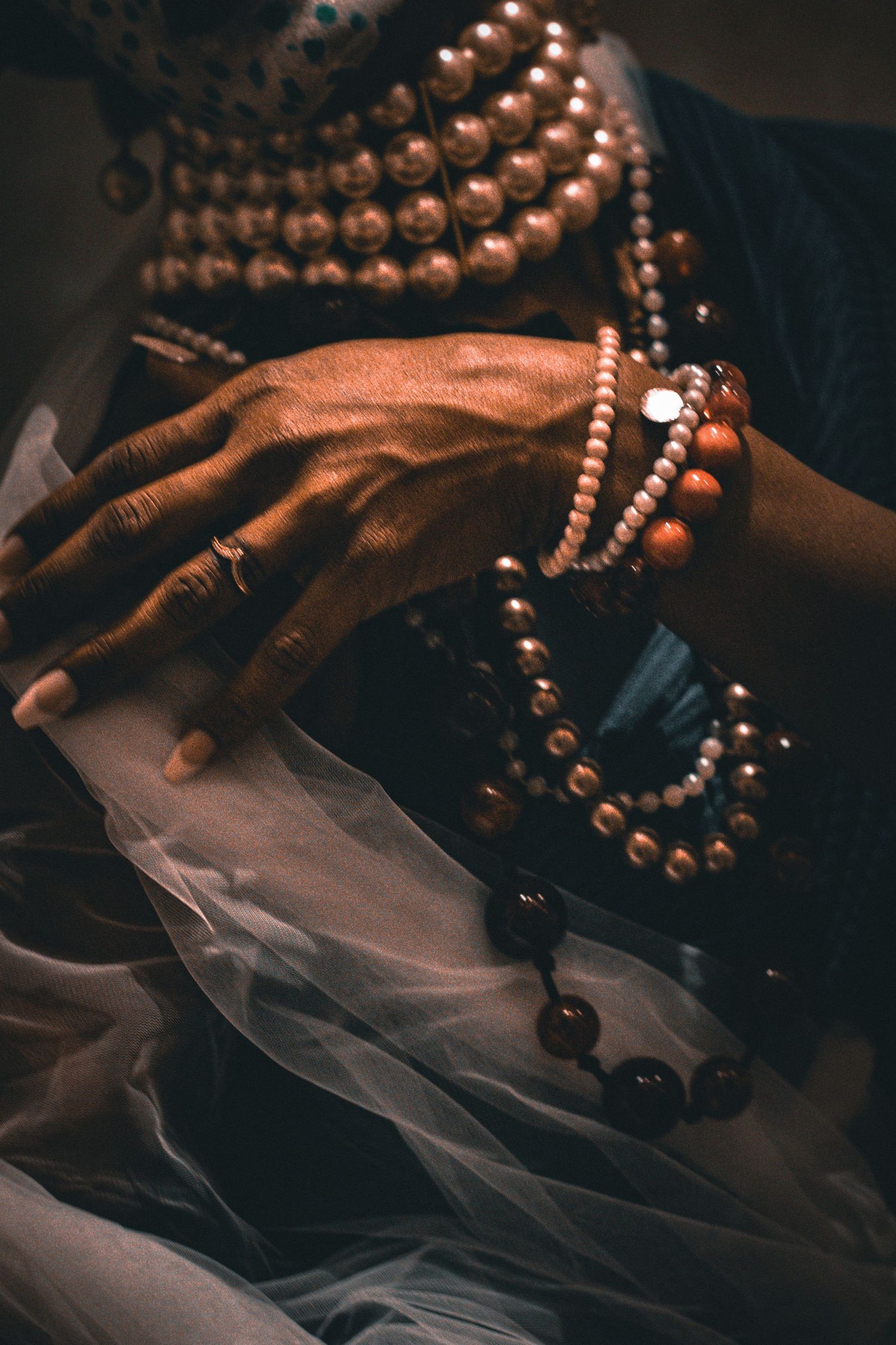 Close-up of hands adorned with pearl and beaded bracelets resting on sheer white fabric.