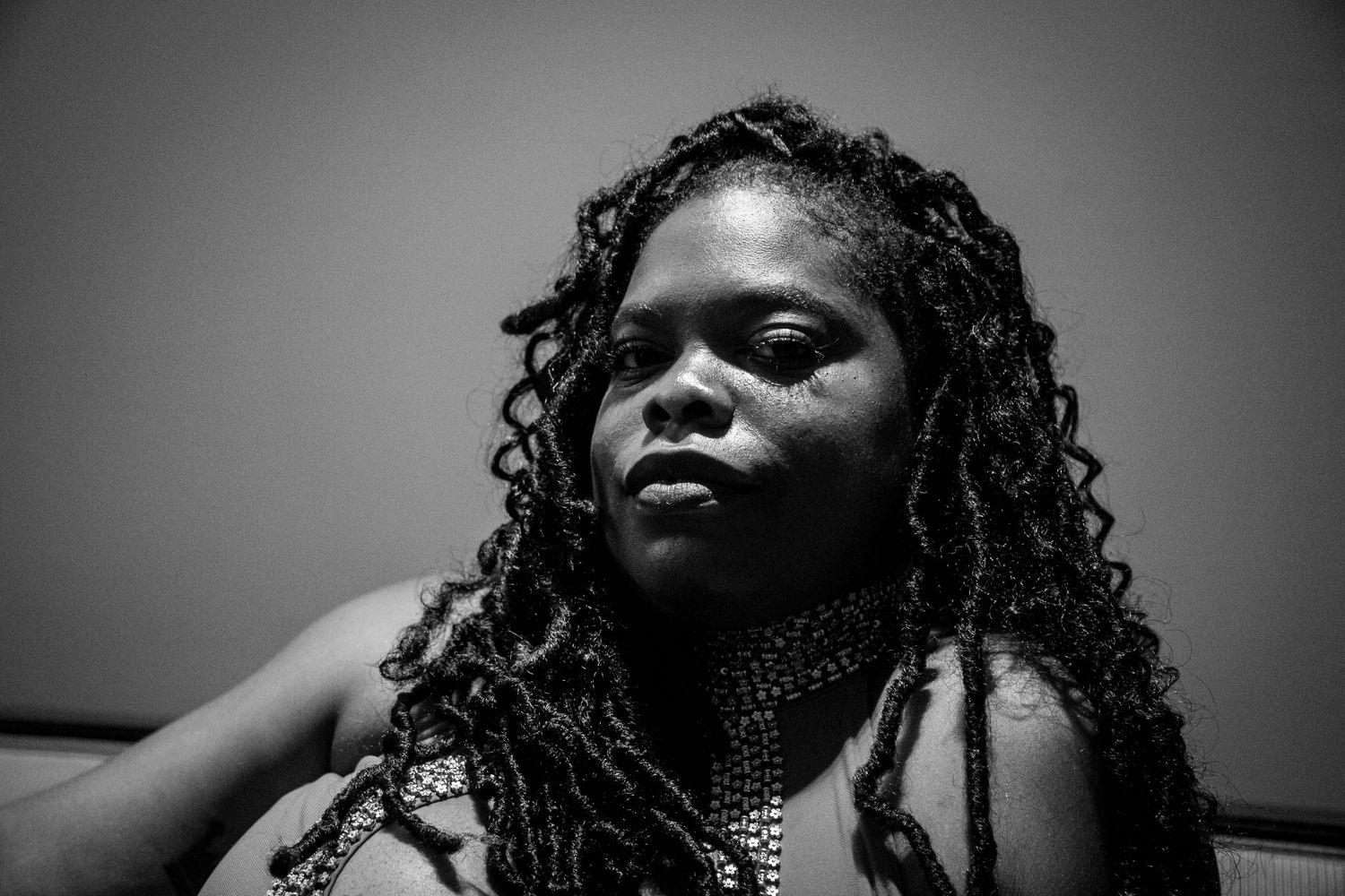 Black and white low-angle portrait of a woman with curly locs wearing beaded jewelry indoors.