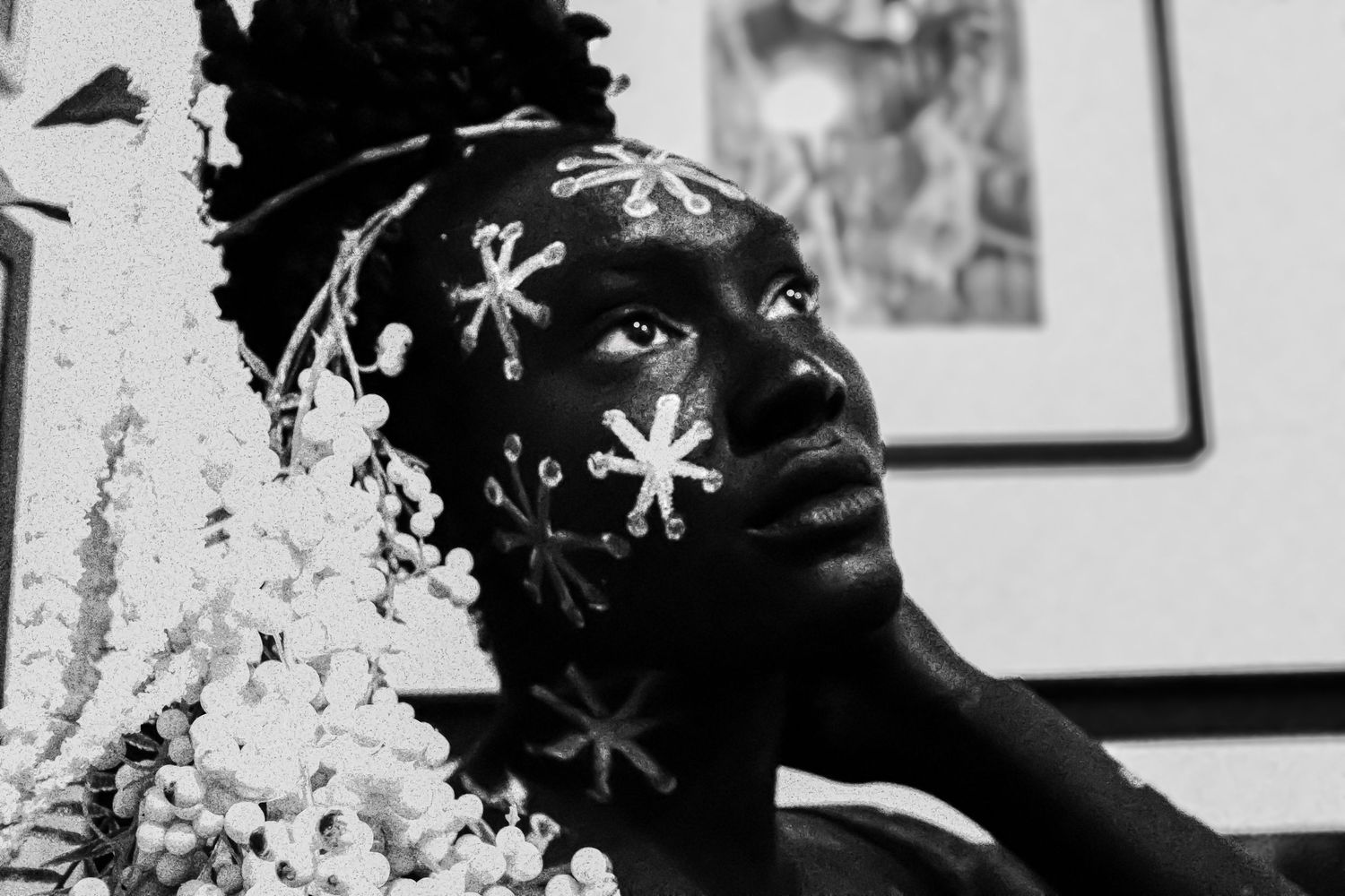Black and white portrait of a person with floral face paint and white flowers in their hair.