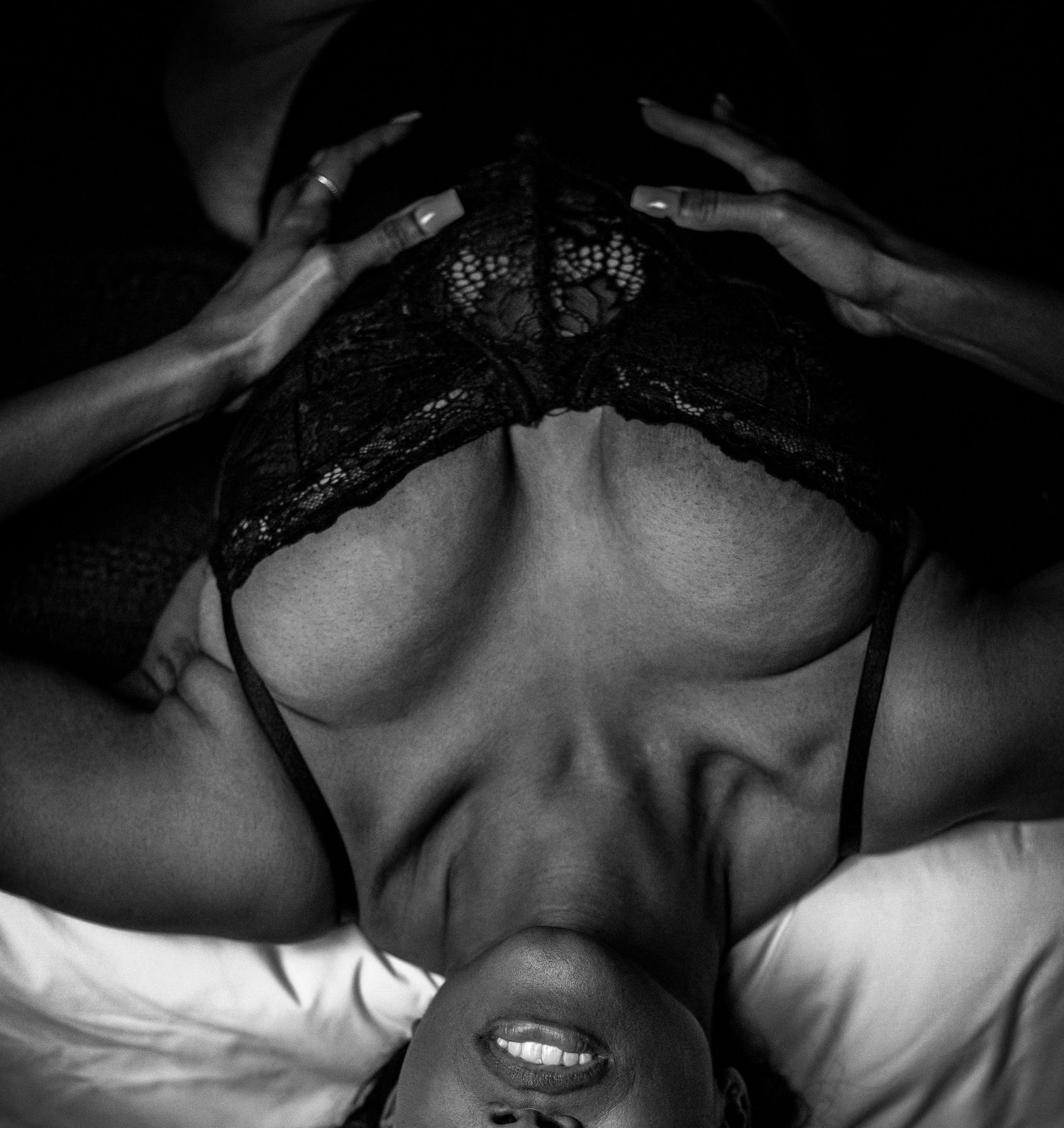 Black and white overhead boudoir photo of a woman in black lace lingerie lying on a bed.