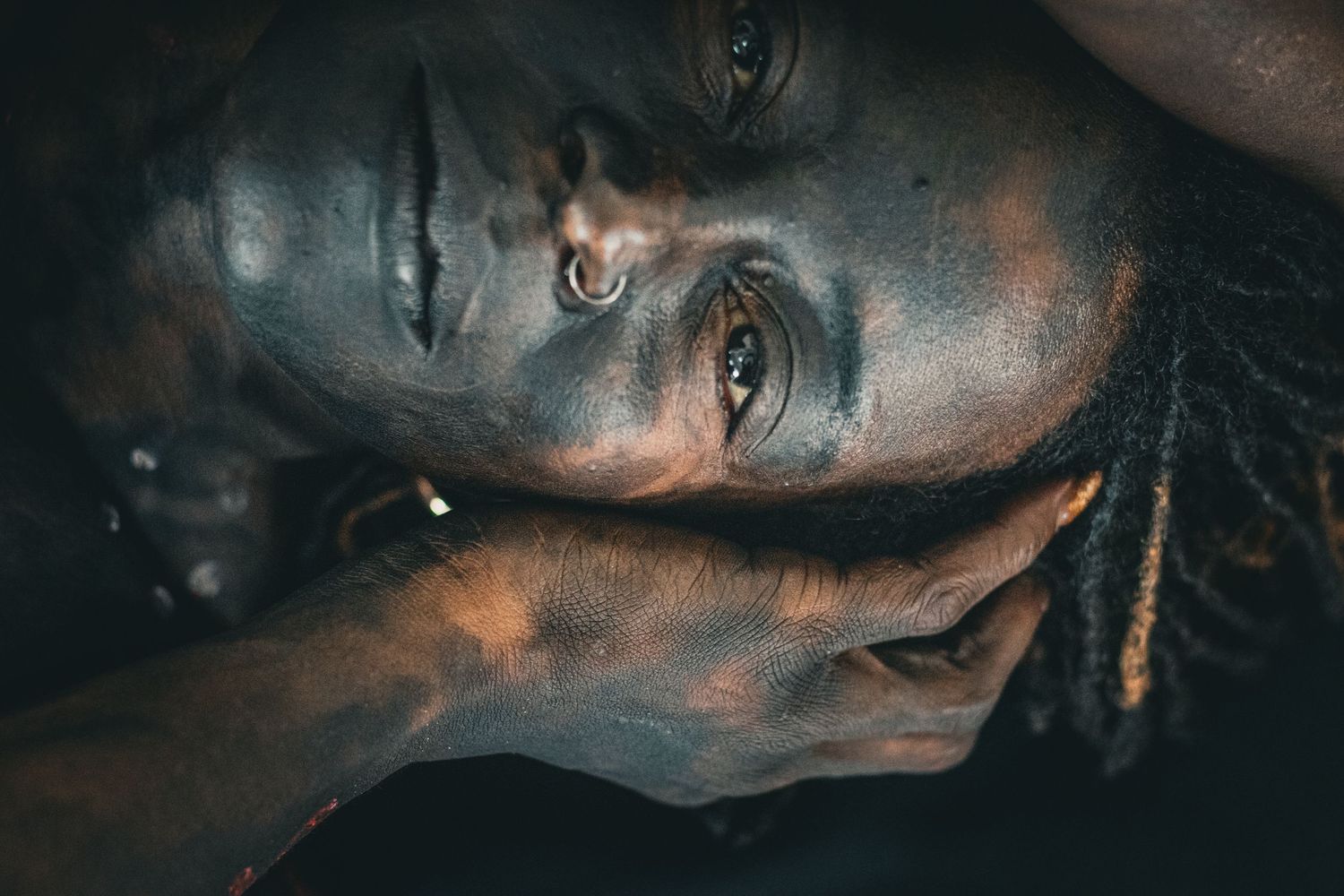 Close-up portrait of person with metallic bronze face paint resting head on hands.