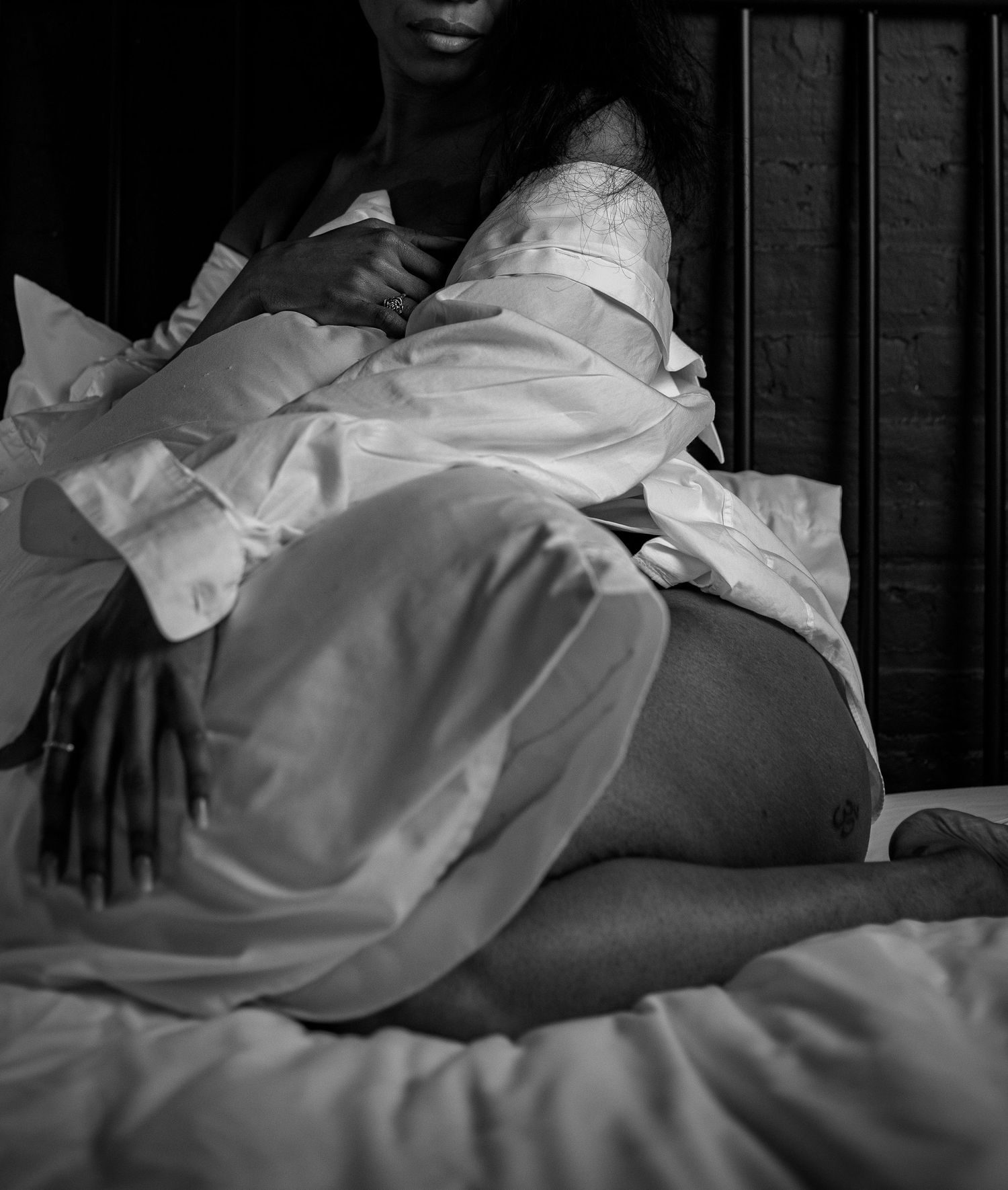 Black and white artistic photo of a woman in white shirt sitting on a bed.