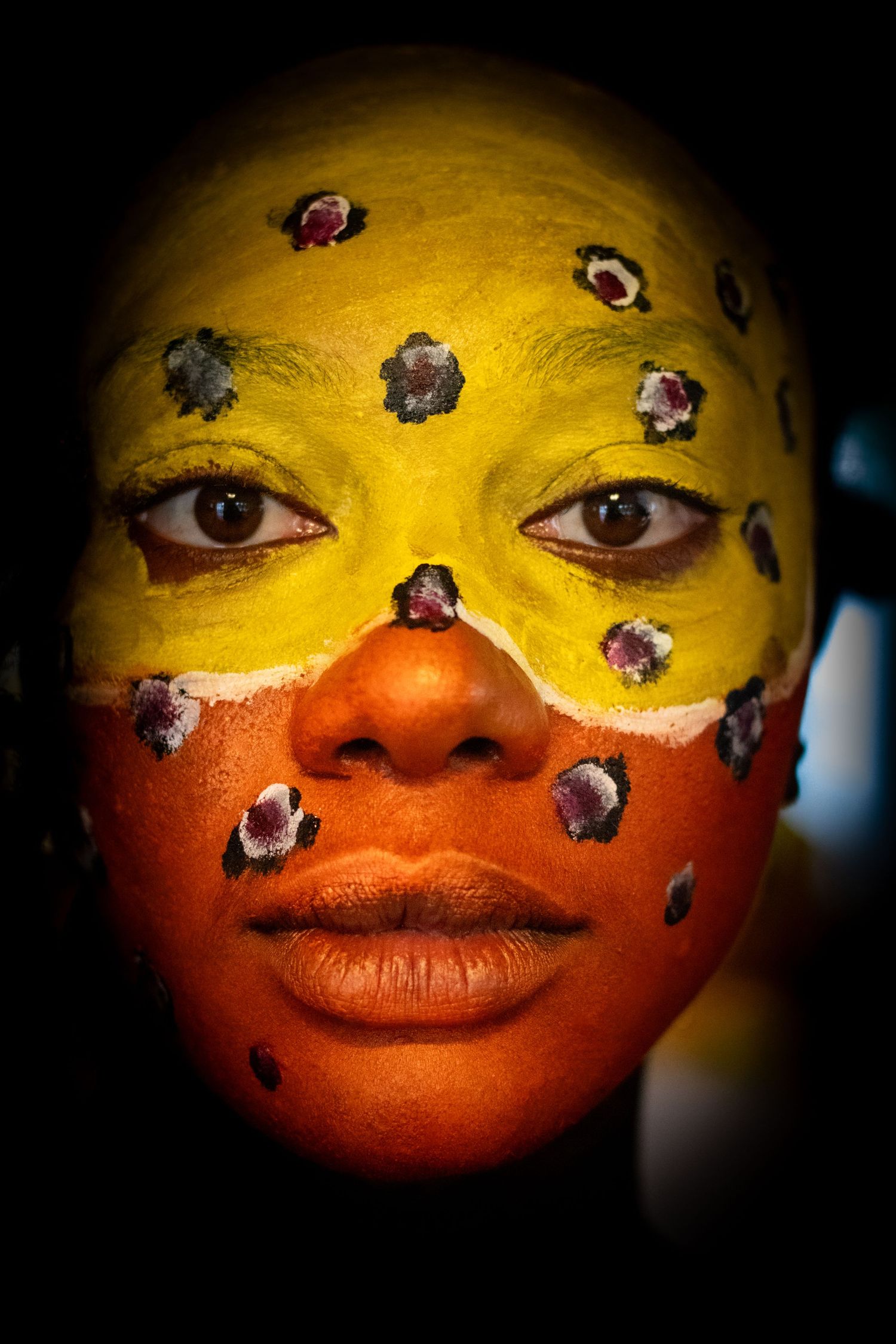 Close-up portrait of woman with vibrant yellow and orange face paint with floral designs.