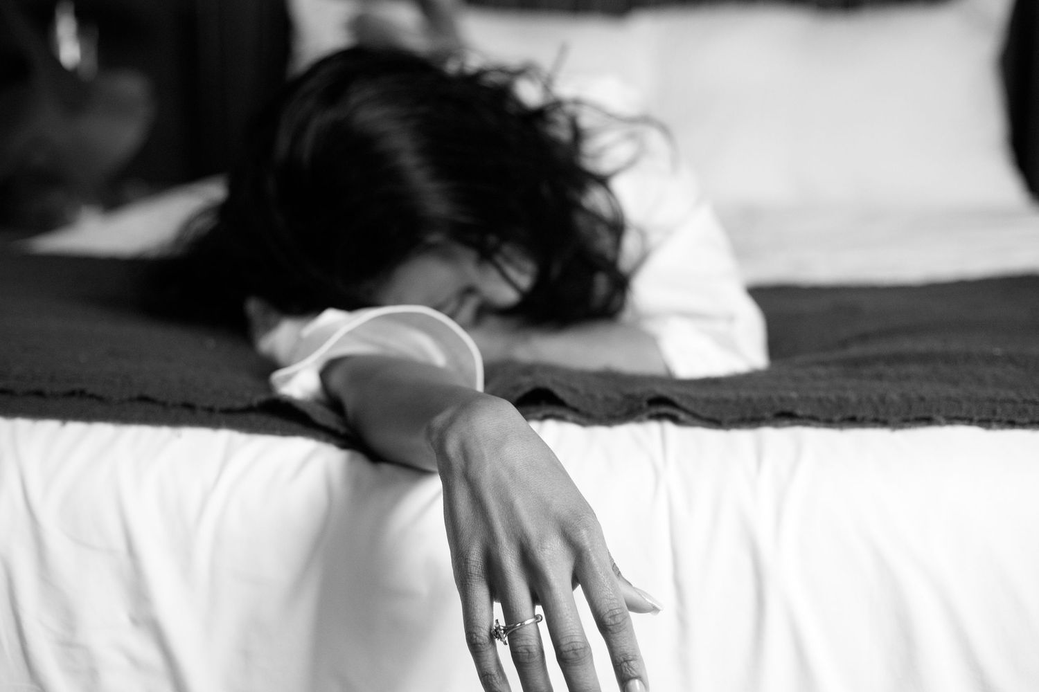 Black and white photo of a woman lying face down on a bed with her hand extended forward.