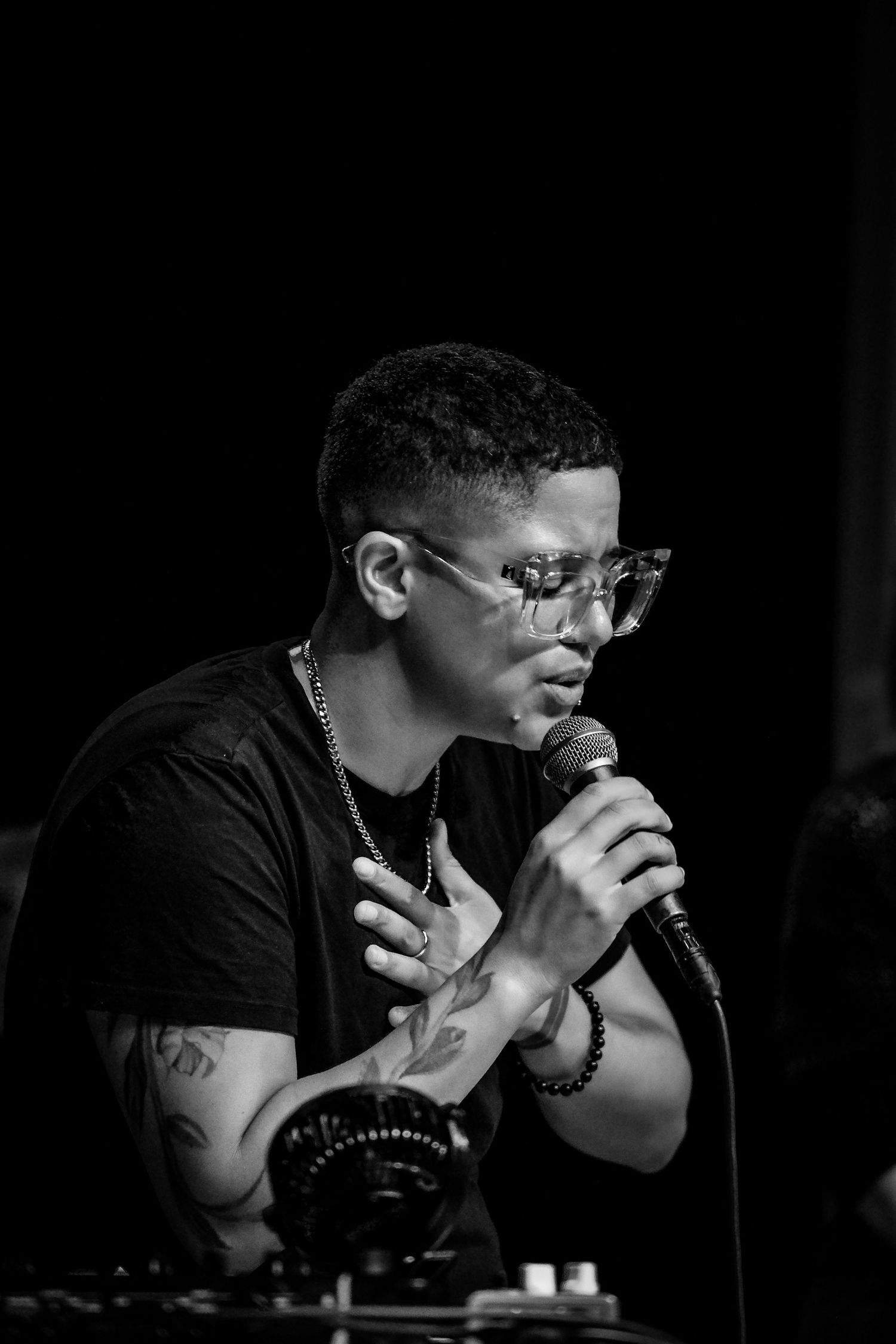 Young male singer with glasses and tattoos performing with microphone in black and white.
