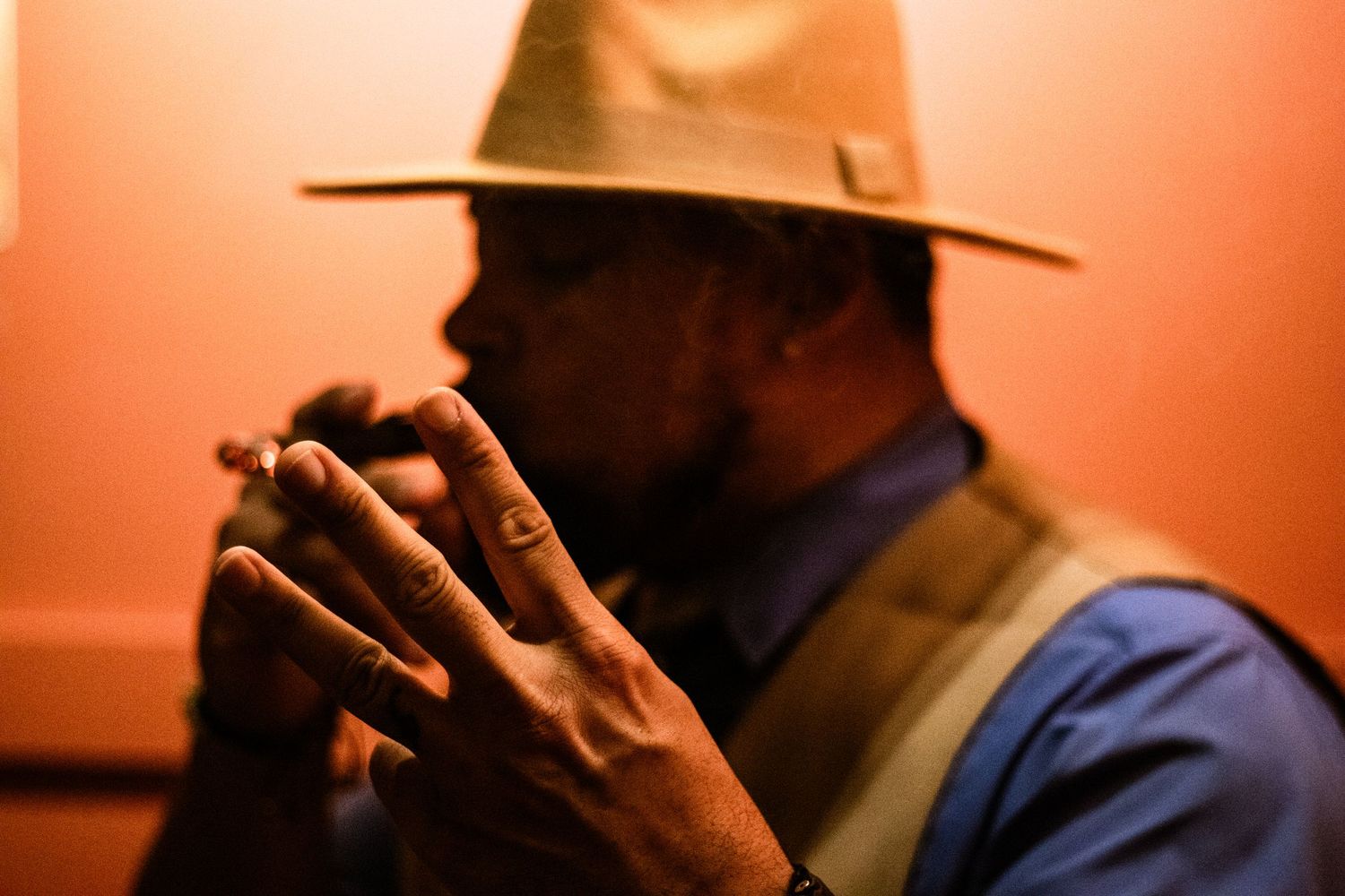 Man in a wide-brim hat smoking a cigar in warm orange ambient indoor lighting.