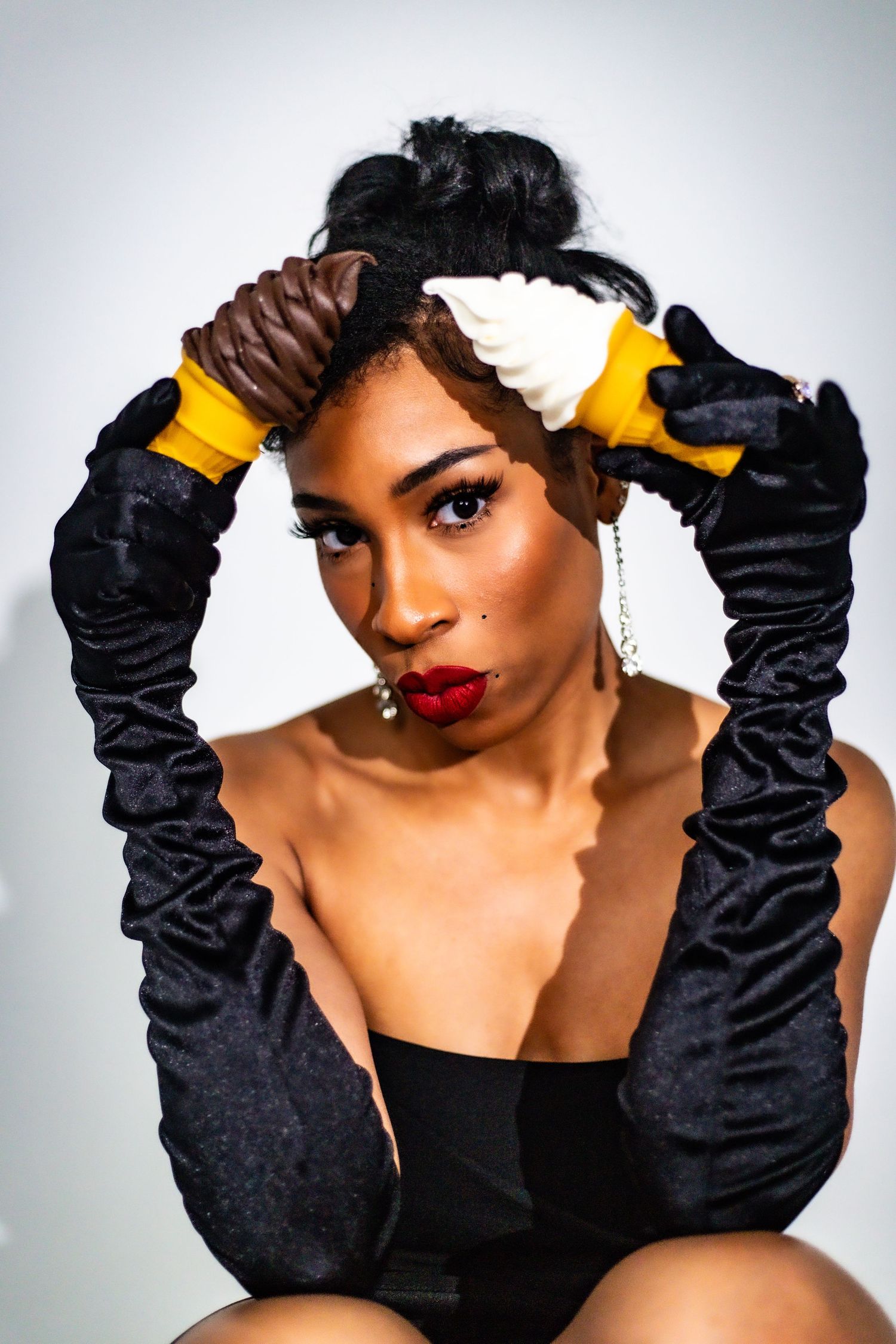 Bold fashion portrait of woman in black corset with yellow gloves and ice cream hair accessories.