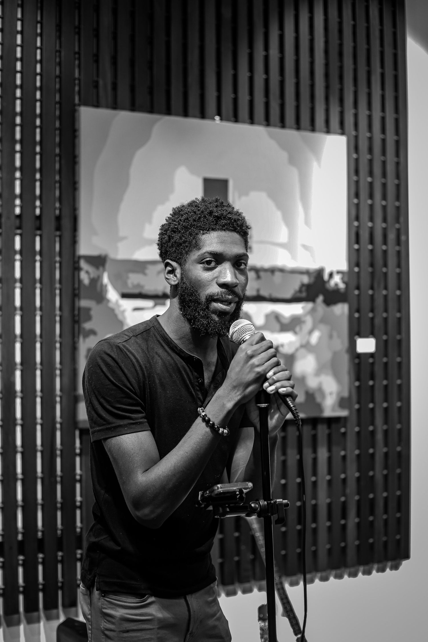 Black and white portrait of a bearded man singing into a microphone at an art gallery.