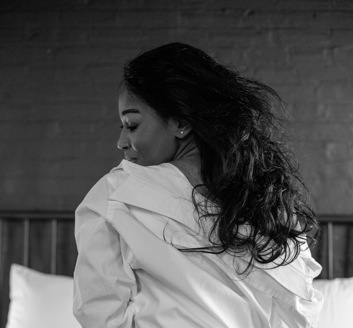 Black and white photo of a woman in a white shirt with flowing dark hair on a bed.