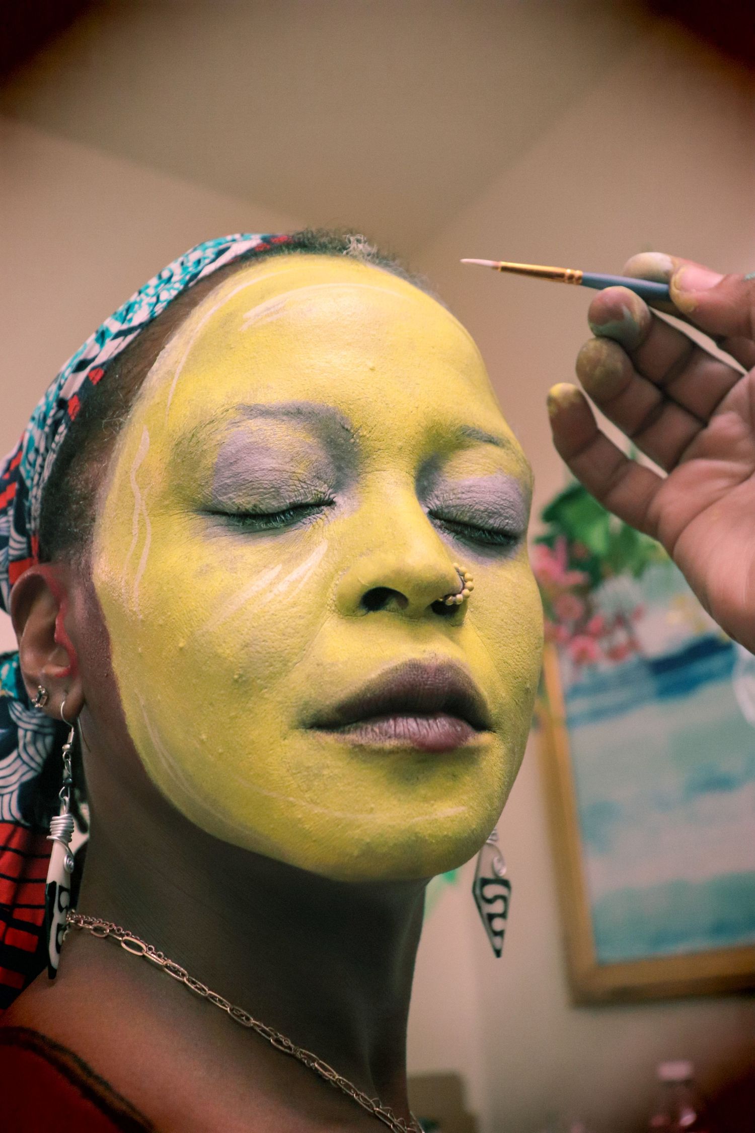 Close-up of a woman having yellow face paint applied with a brush during a makeup session.