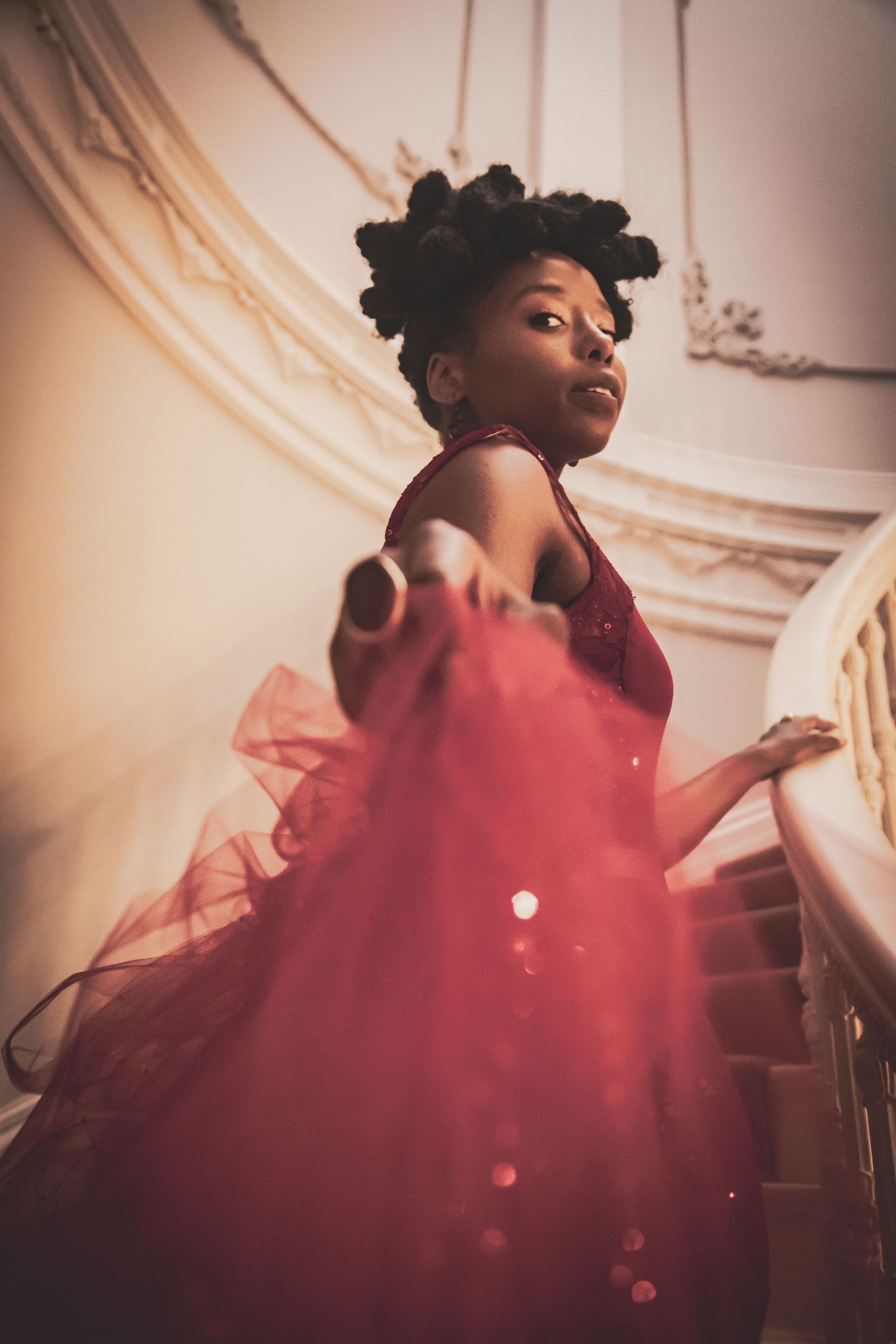 Young woman in a stunning red sequined ball gown descending an ornate staircase.
