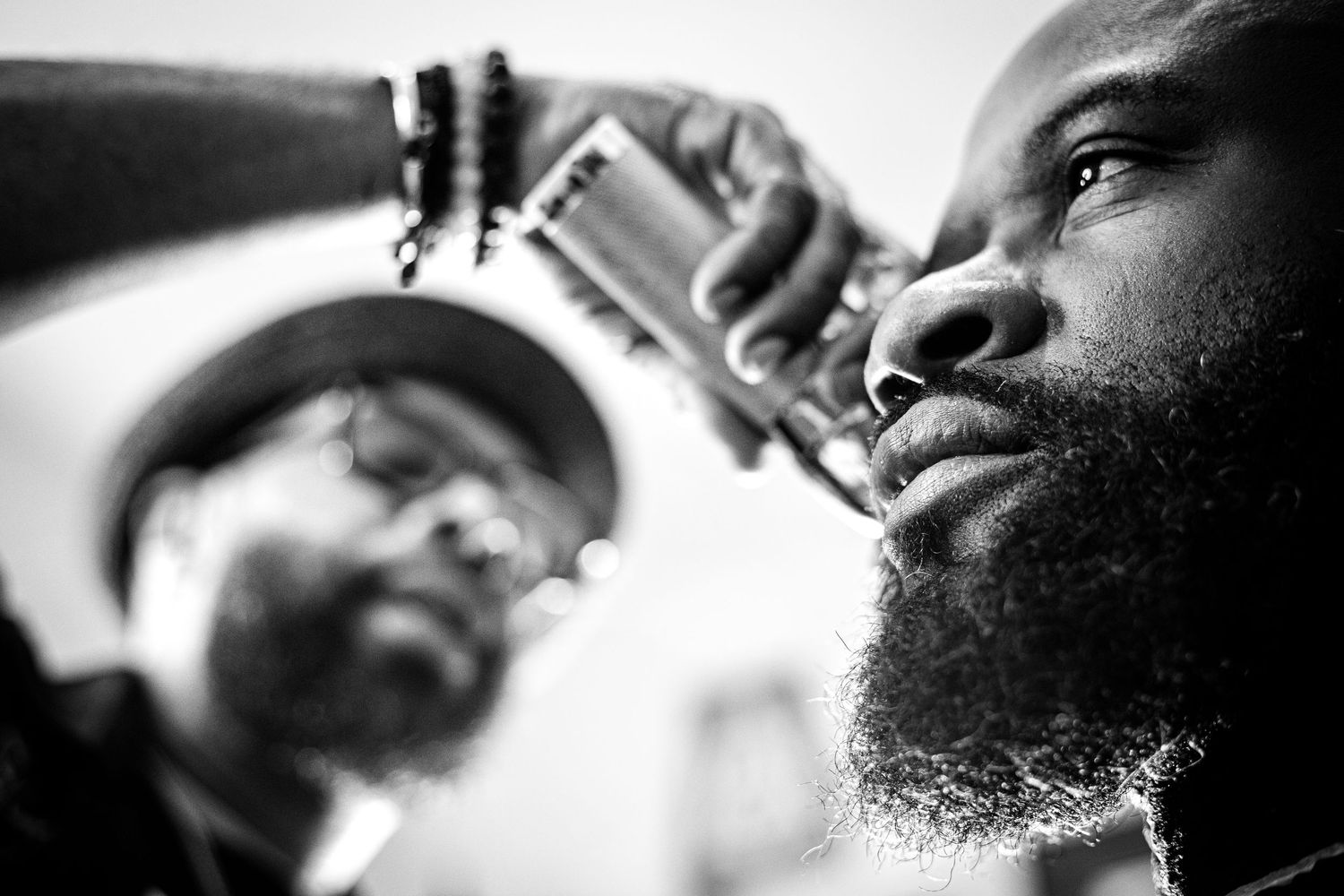 Black and white photo of a barber trimming a mans beard with electric clippers.
