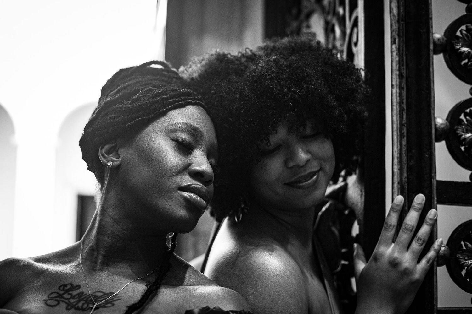 Black and white intimate portrait of two Black women leaning close together near ornate door.