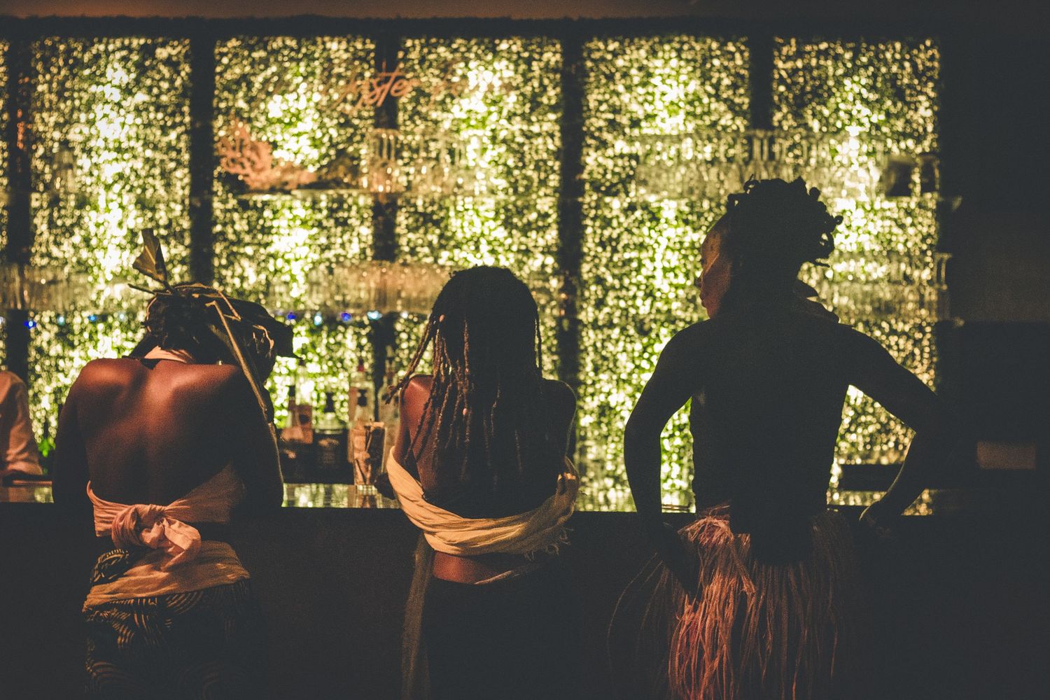 Three women silhouetted against glowing fairy lights at a bar.