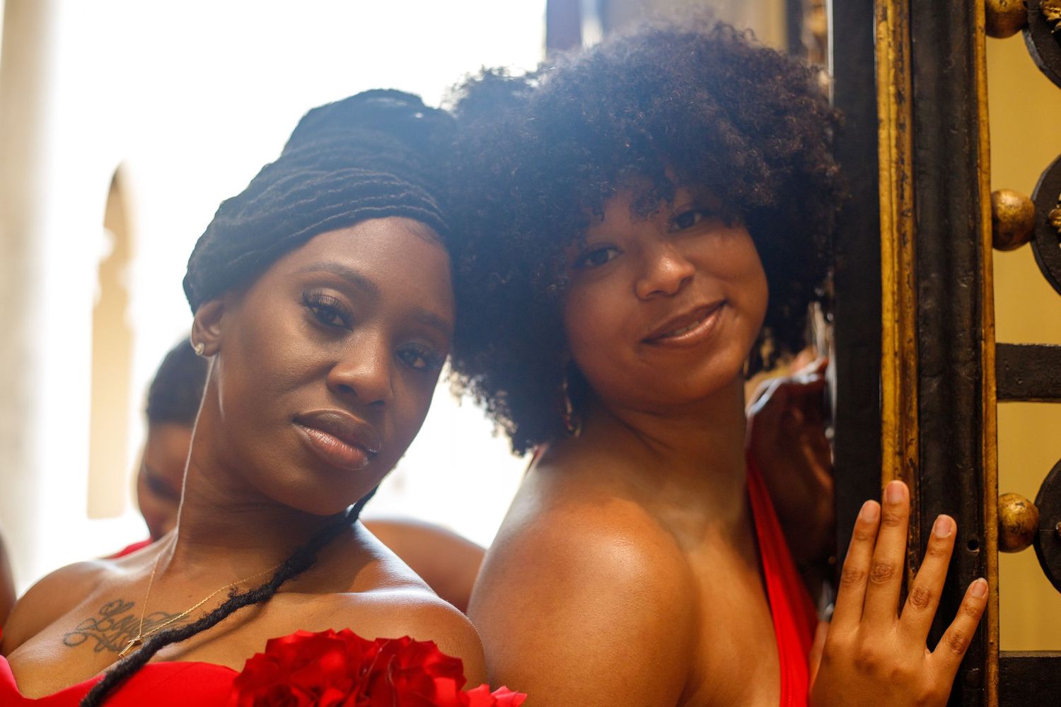 Two women in red outfits posing closely together near decorative golden door frame.