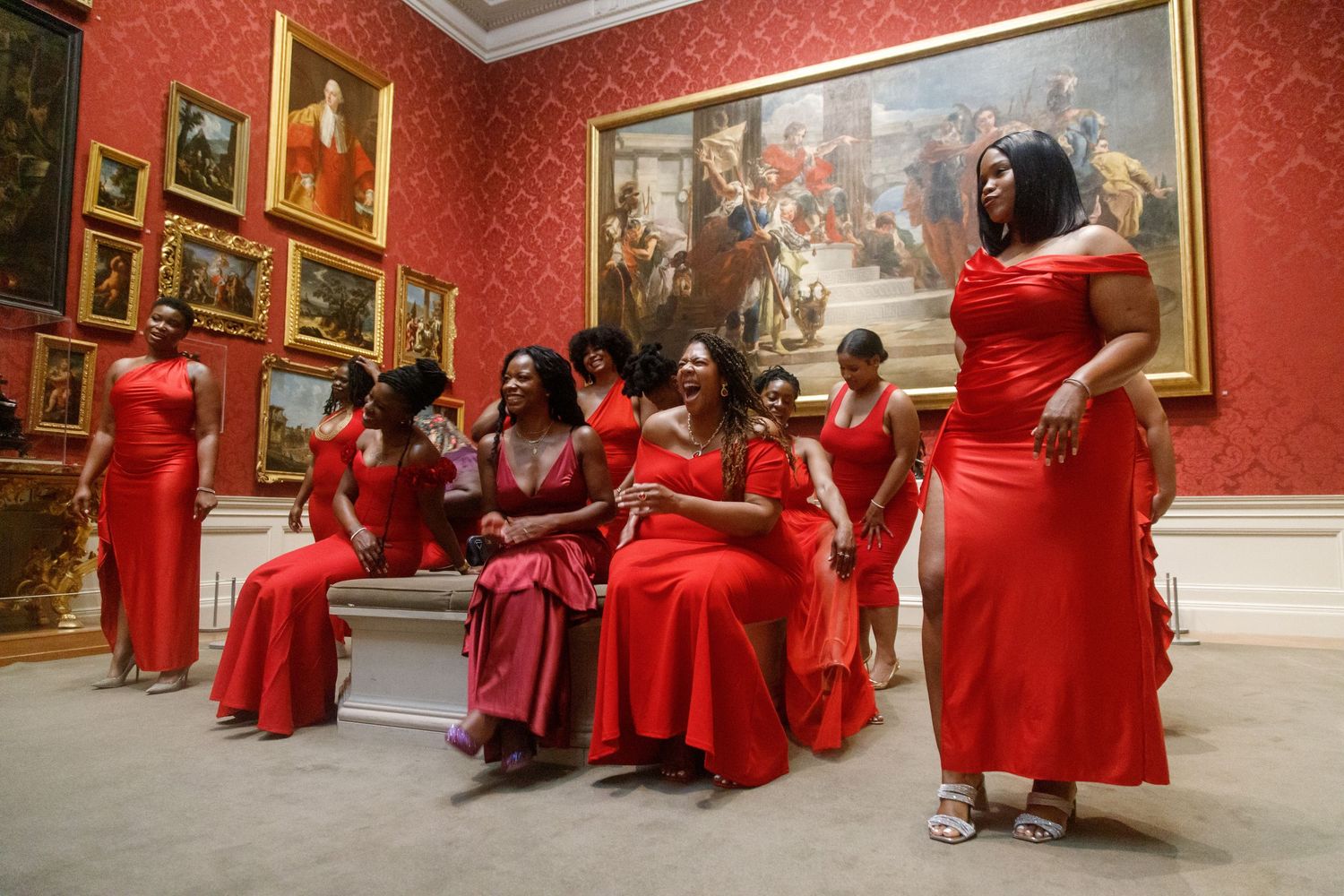 Women in red dresses relaxing in classic art museum gallery.