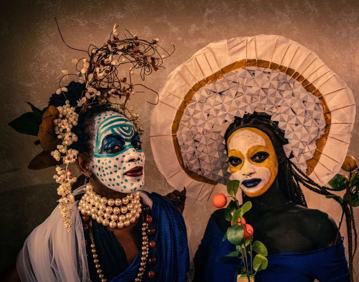 Two performers in elaborate tribal face paint, beaded jewelry, and decorative headdresses pose together.