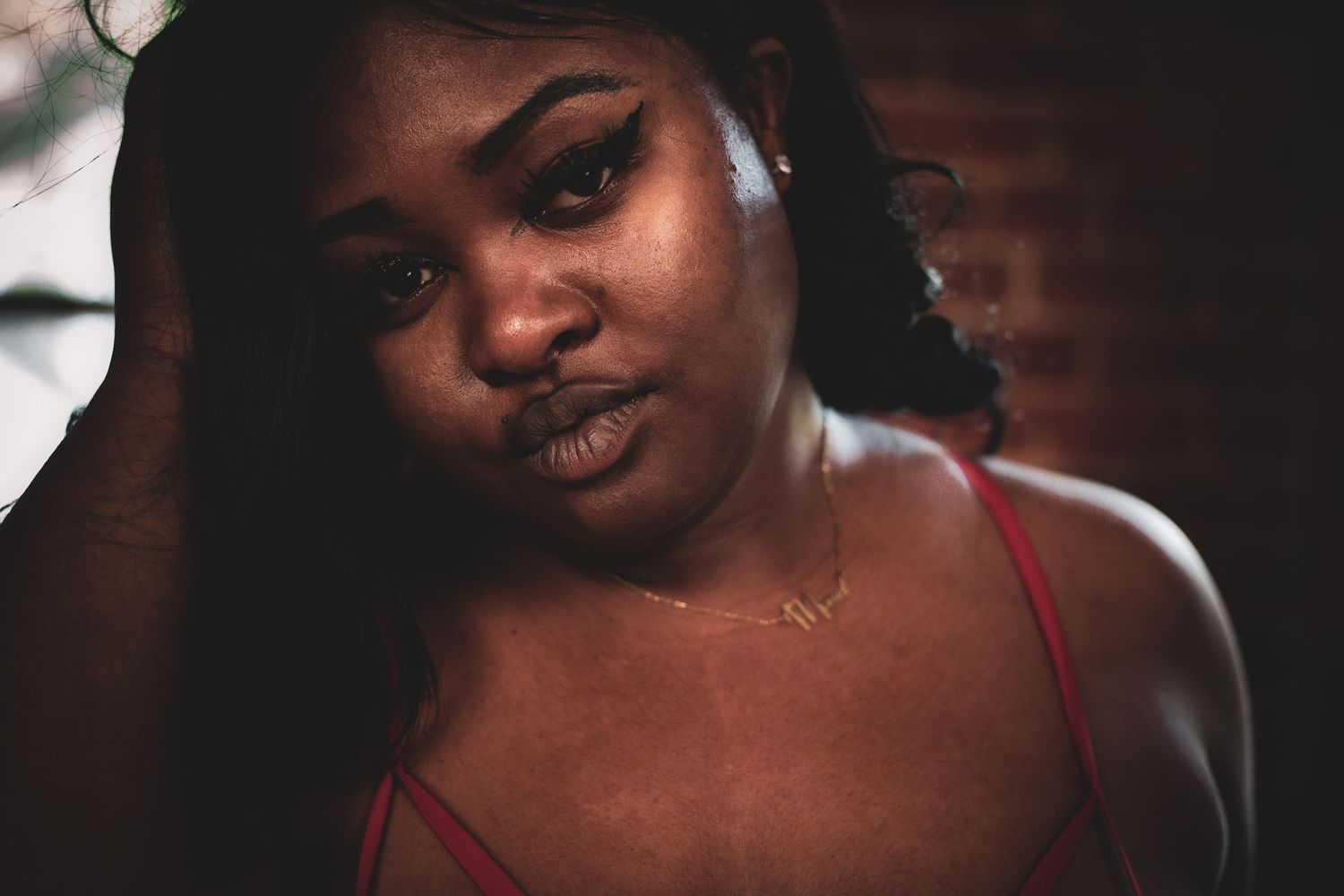 Close-up portrait of a young Black woman in red lingerie with a soft, confident gaze in warm lighting.