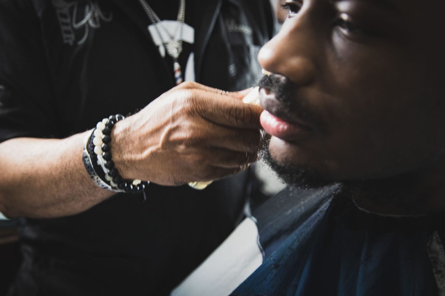 Close-up of a barbers hand trimming a young mans beard with precision grooming tools.