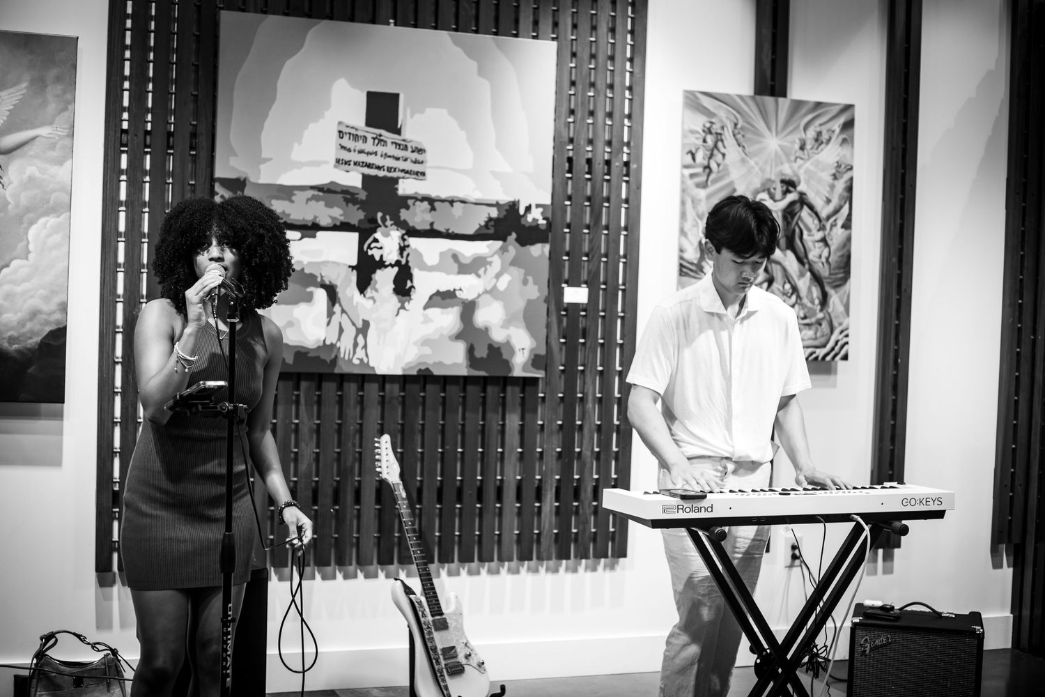 Black and white image of female singer and male keyboardist performing in art gallery.