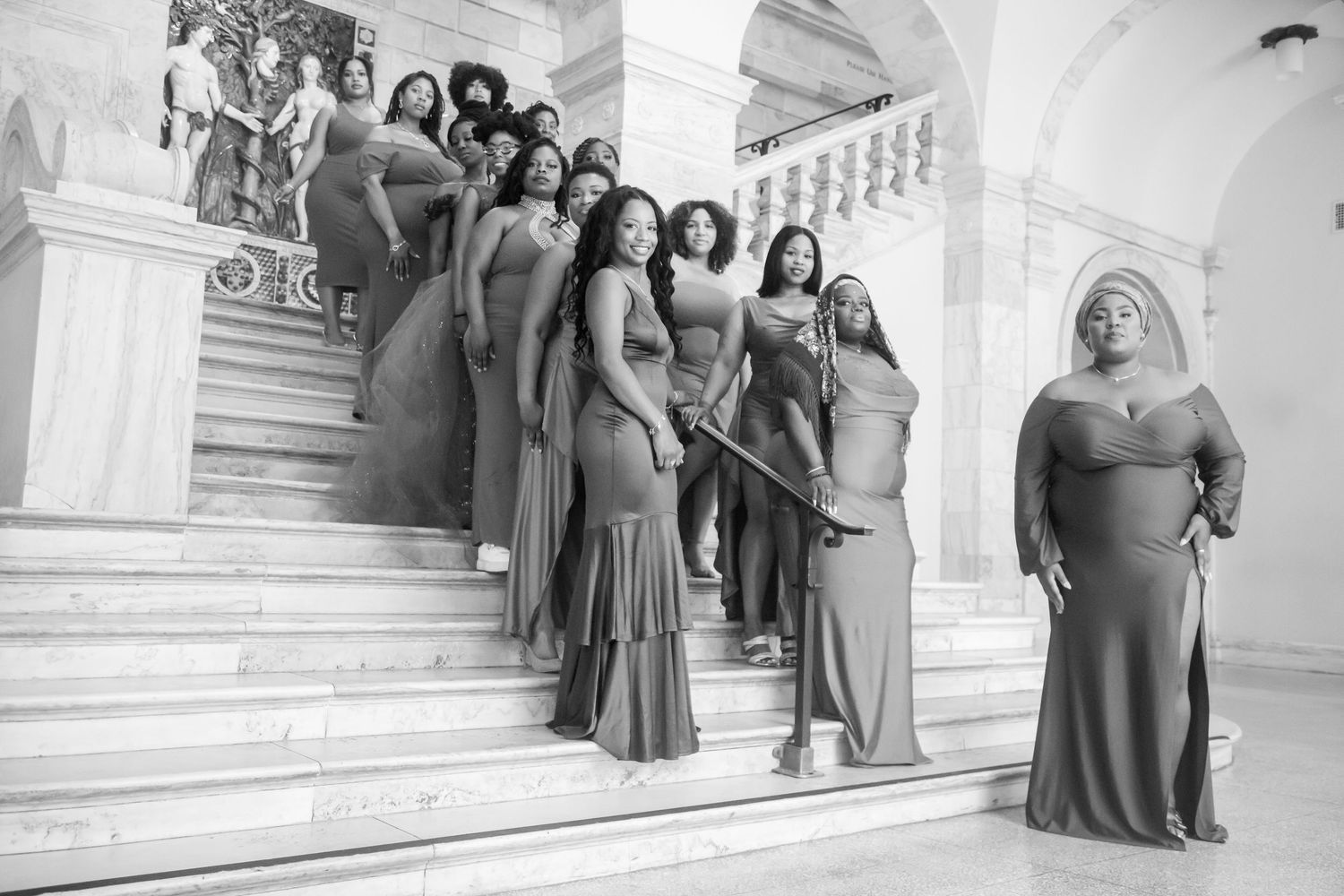 Group of women in matching gray gowns posing on marble staircase.