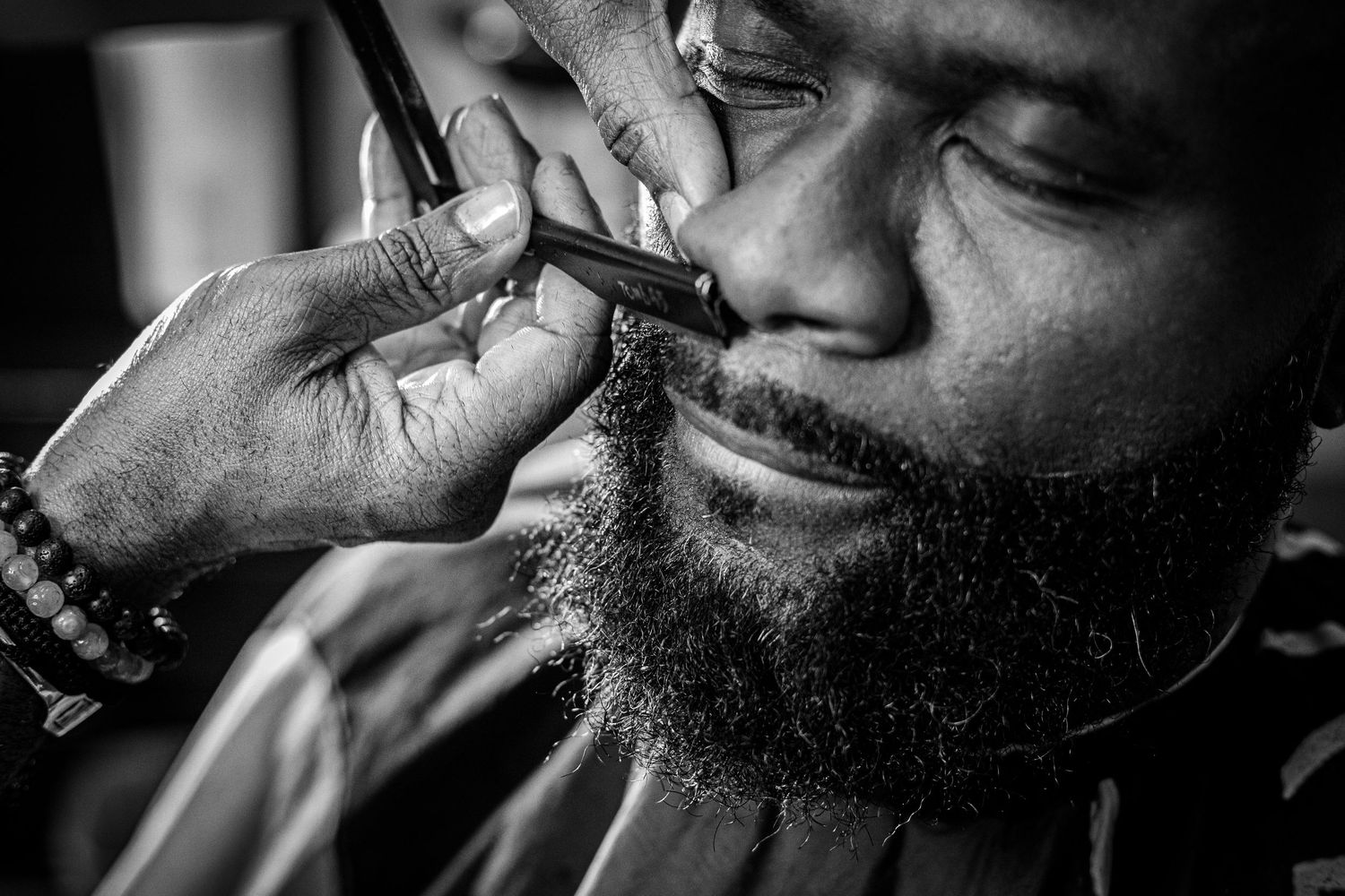 Black and white close-up of barber trimming a mans beard with a straight razor.
