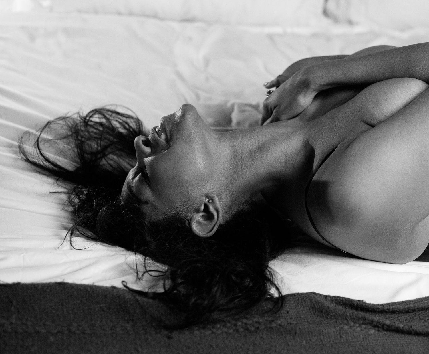 Black and white artistic photo of a woman lying on white bedding looking upward.