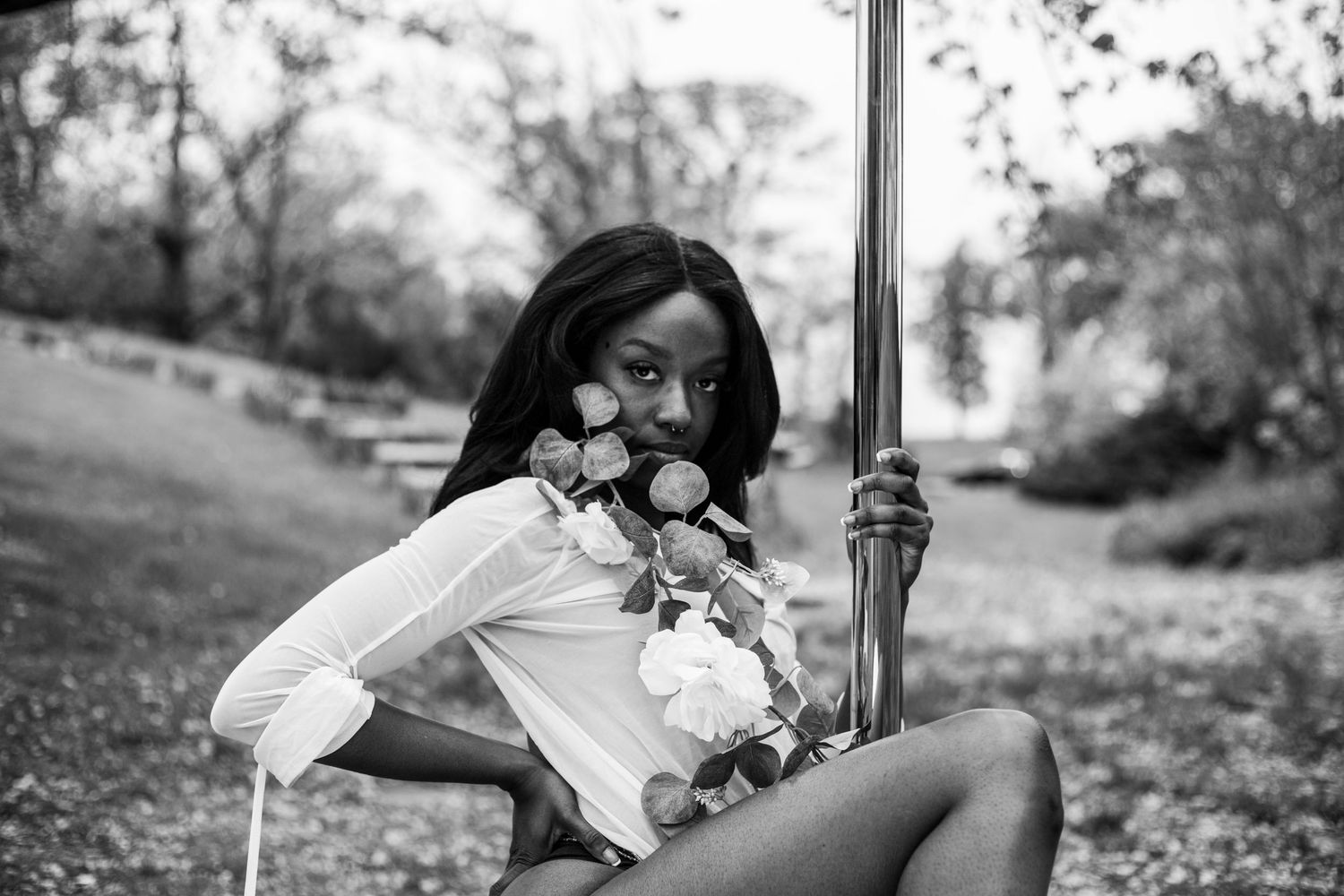 Black and white portrait of woman holding flowers beside a pole in a park.