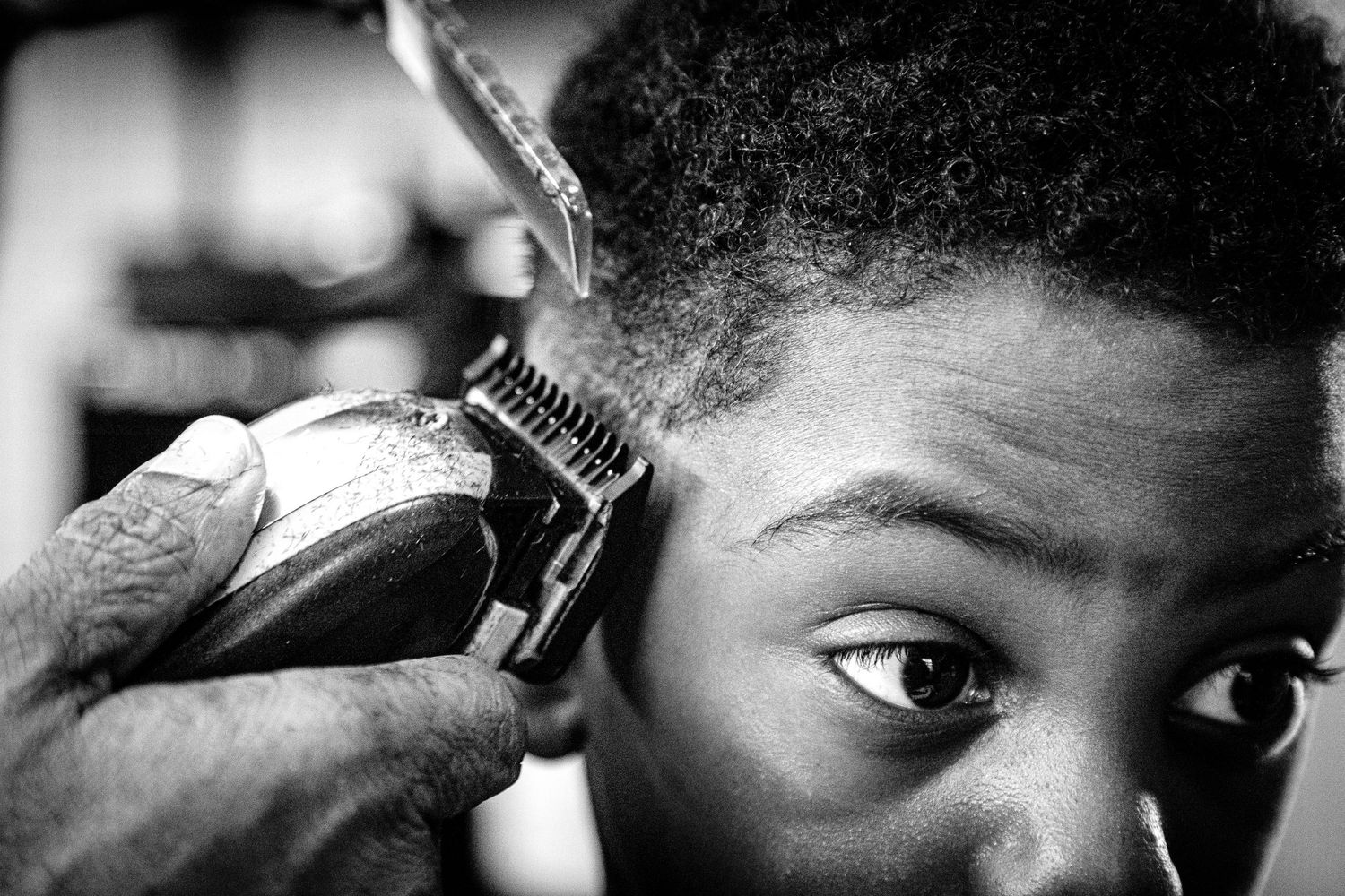 Close-up black and white photo of a barber using clippers on a young boys hair.