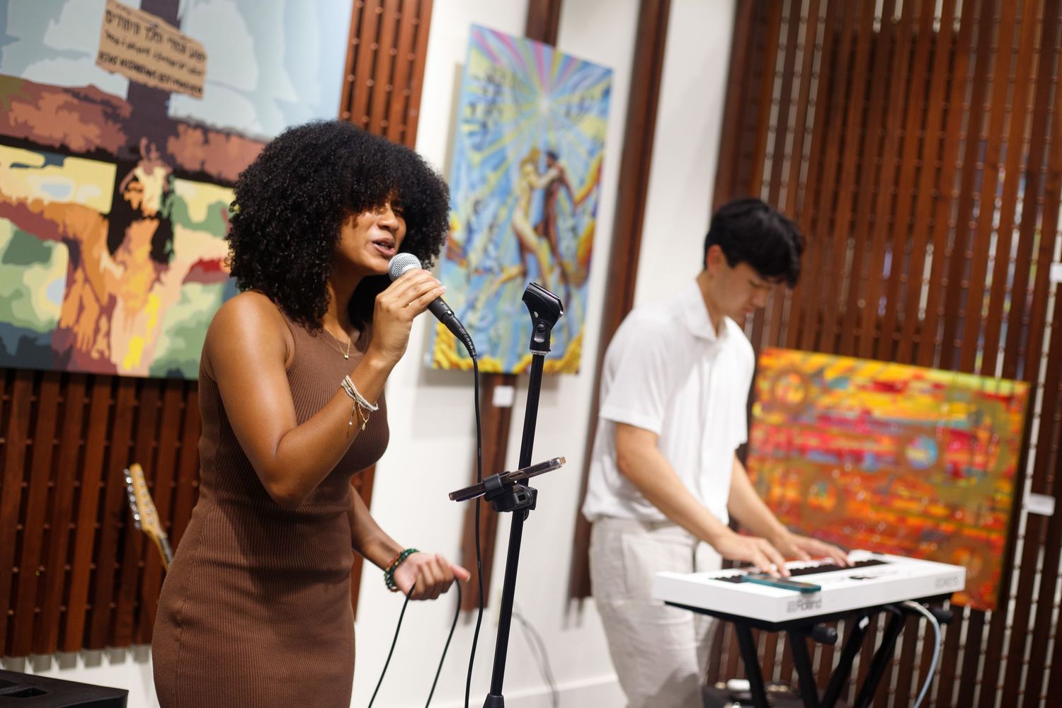 Woman with natural afro hair singing into microphone at indoor art gallery performance.