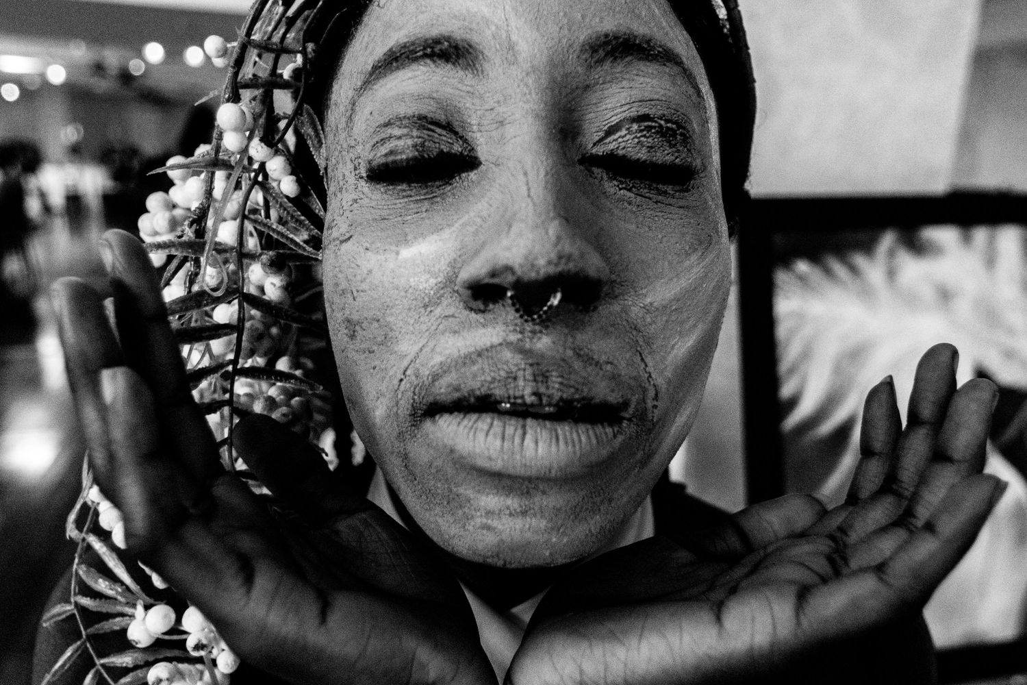 Black and white close-up portrait of woman with white face paint framing face with hands.