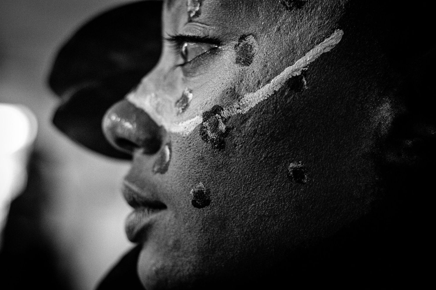 Black and white portrait of a woman's side profile with ceremonial face paint and decorative dots on their cheek.