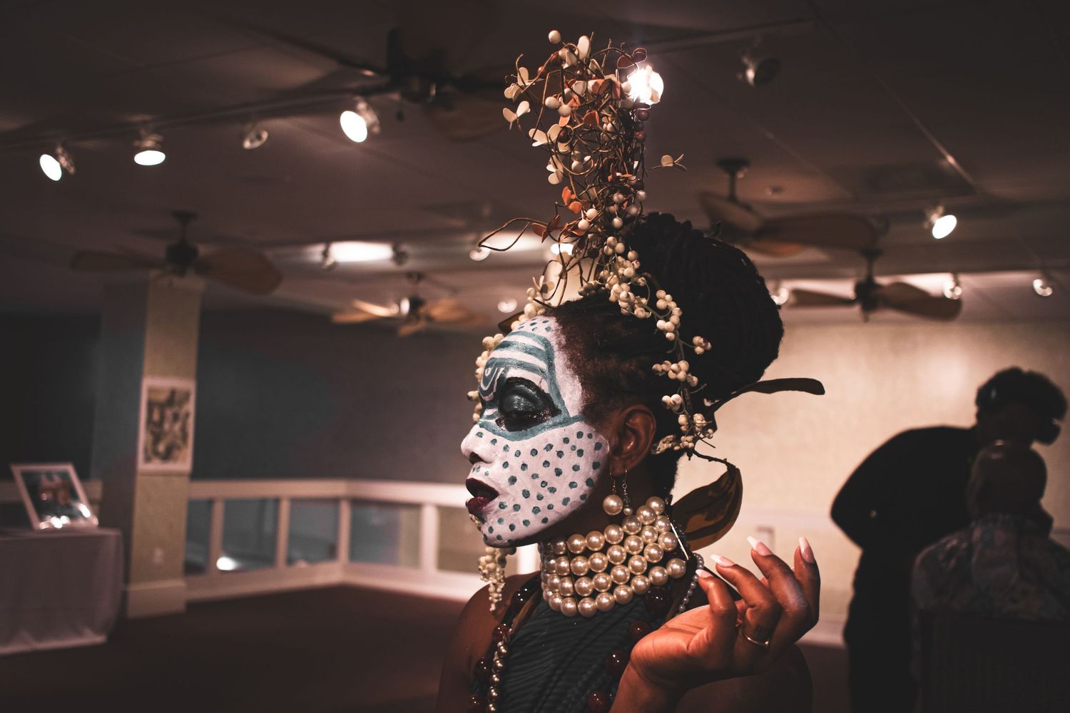 Performer in elaborate headdress and face paint at an indoor art gallery event.