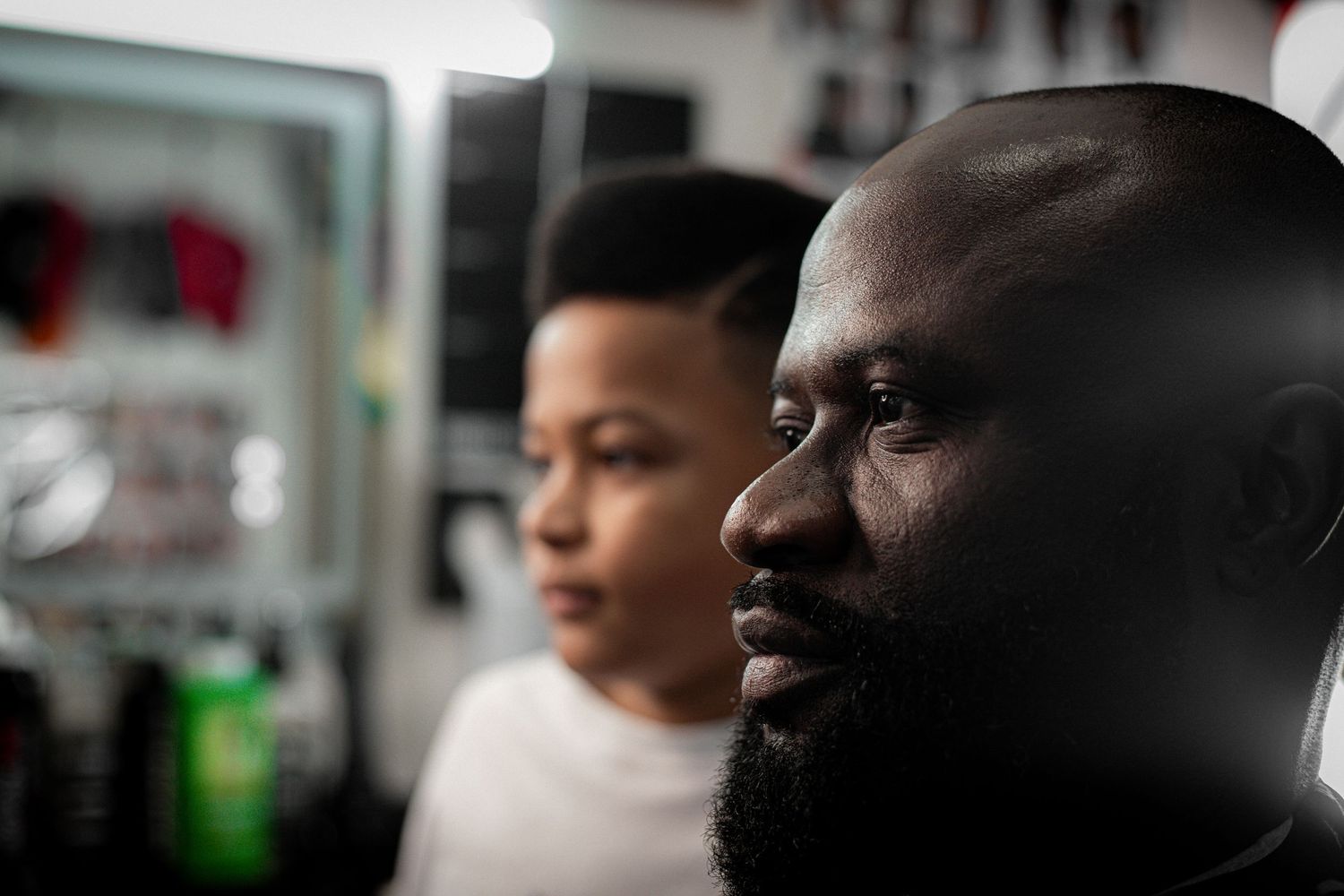 Close-up portrait of a bearded man and young boy in a barbershop setting.