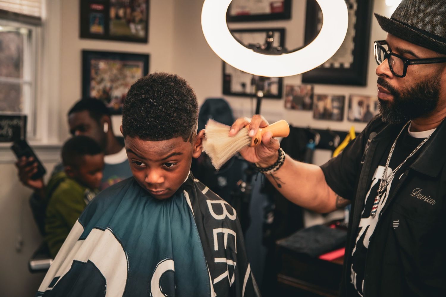 A barber uses a comb and clippers to cut a young boys hair under bright ring light.