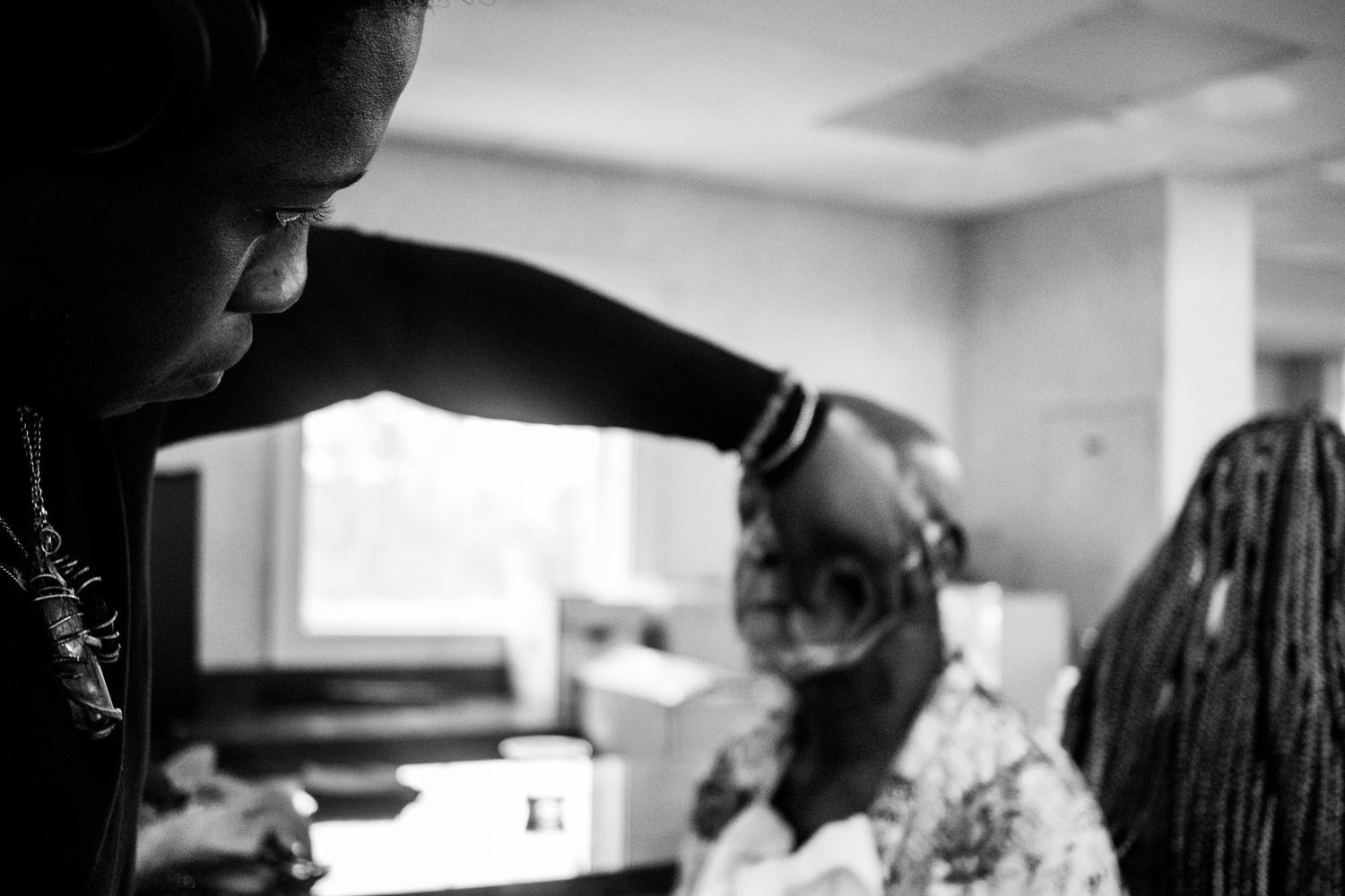 Black and white behind-the-scenes photo of a hairstylist working on a client in a bright studio.