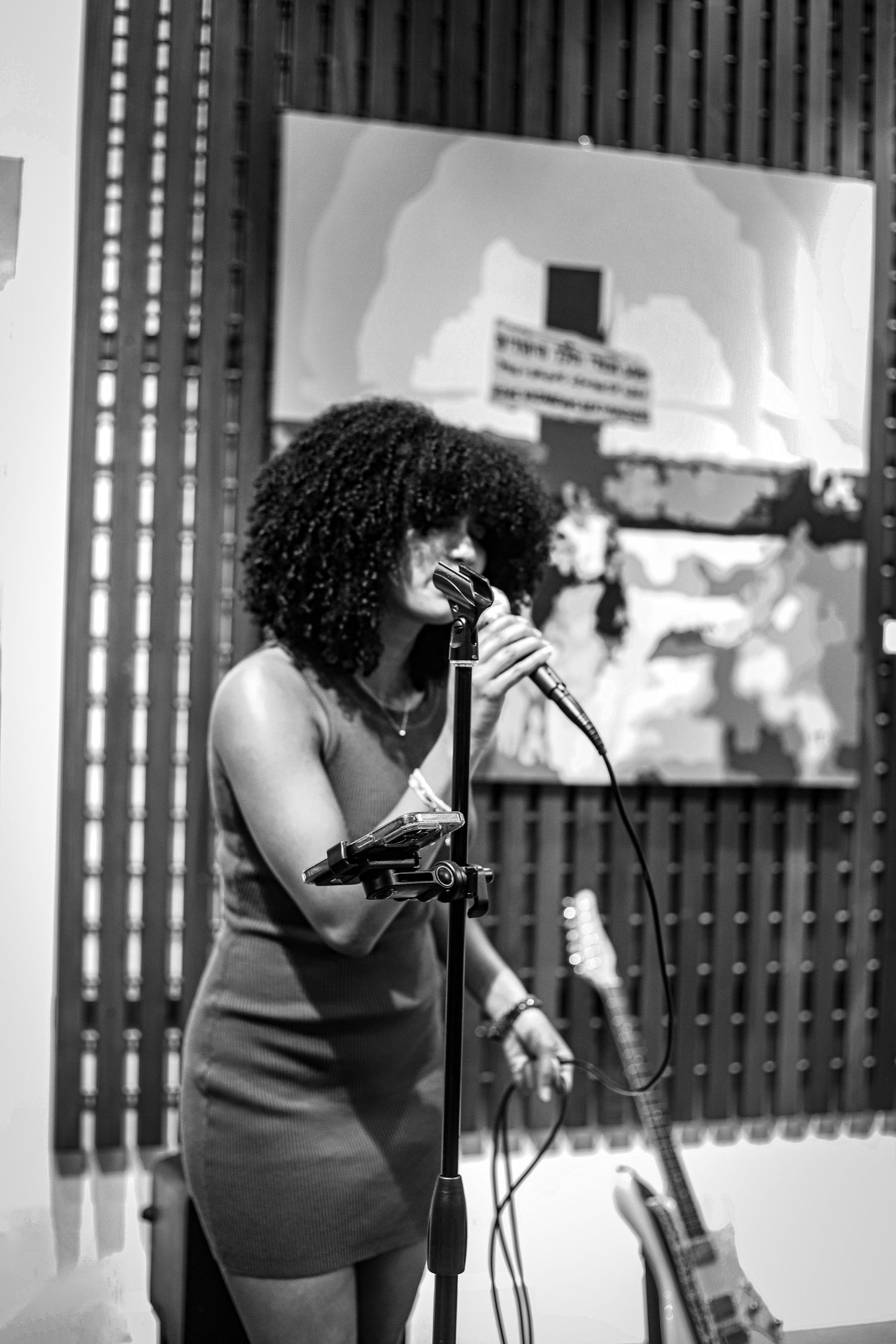 Black and white portrait of woman with afro singing into microphone at live event.