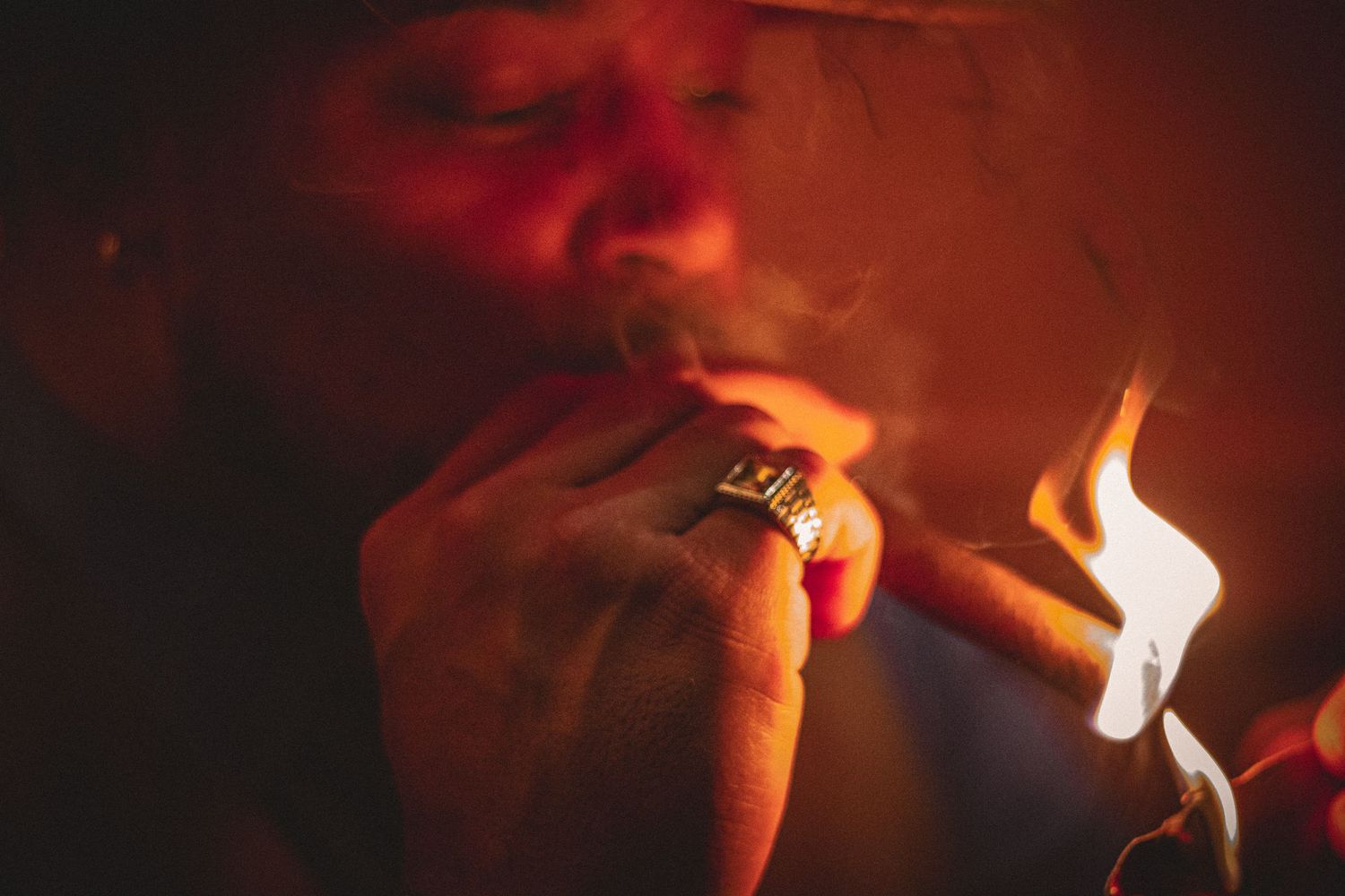Close-up of a person lighting a cigar with a flame lighter in warm dramatic lighting.