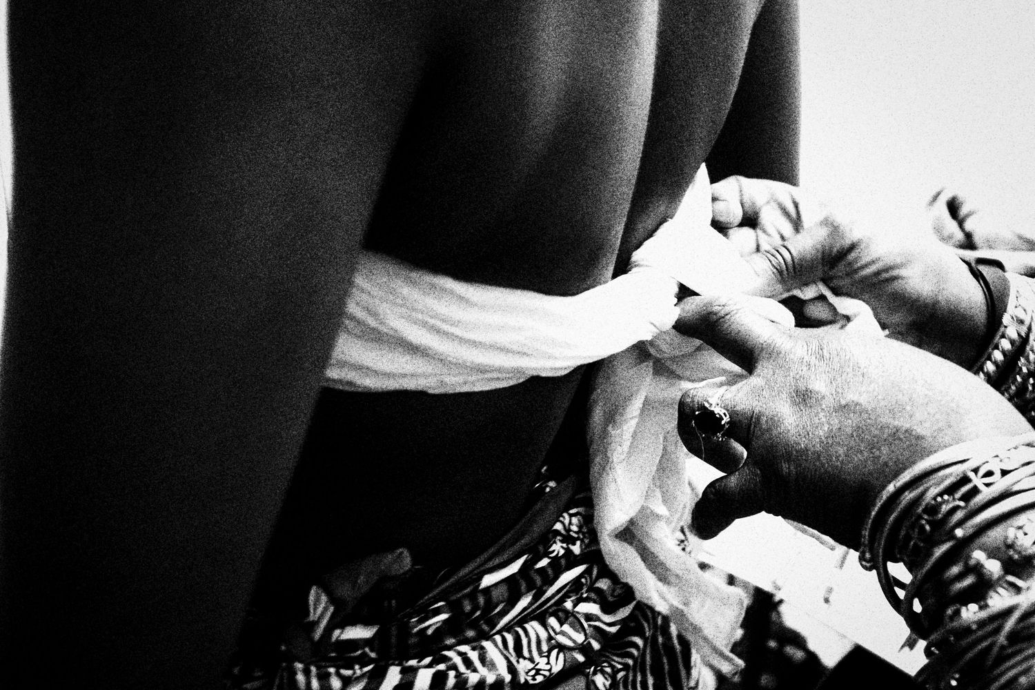 Black and white image of hands wrapping white fabric around a persons waist during a costume preparation.