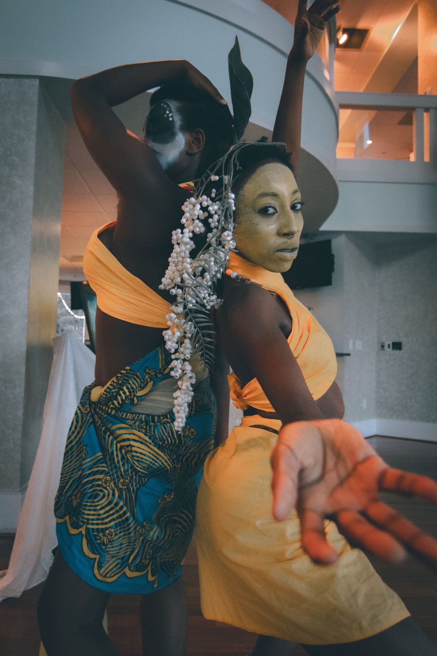 Two performers in orange and African print costumes pose dynamically during indoor cultural performance.
