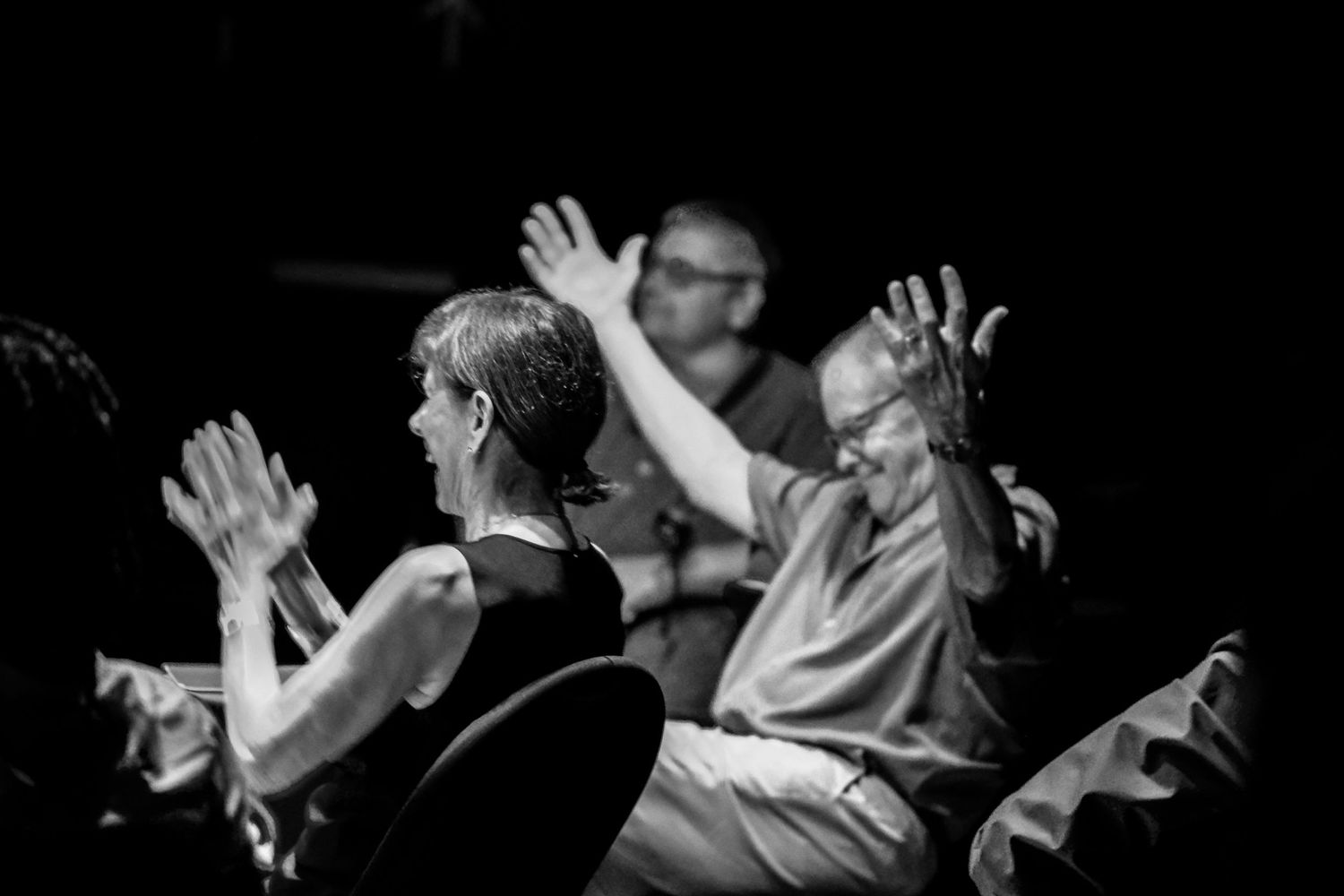 Audience members raise their hands enthusiastically at a live music event in black and white.