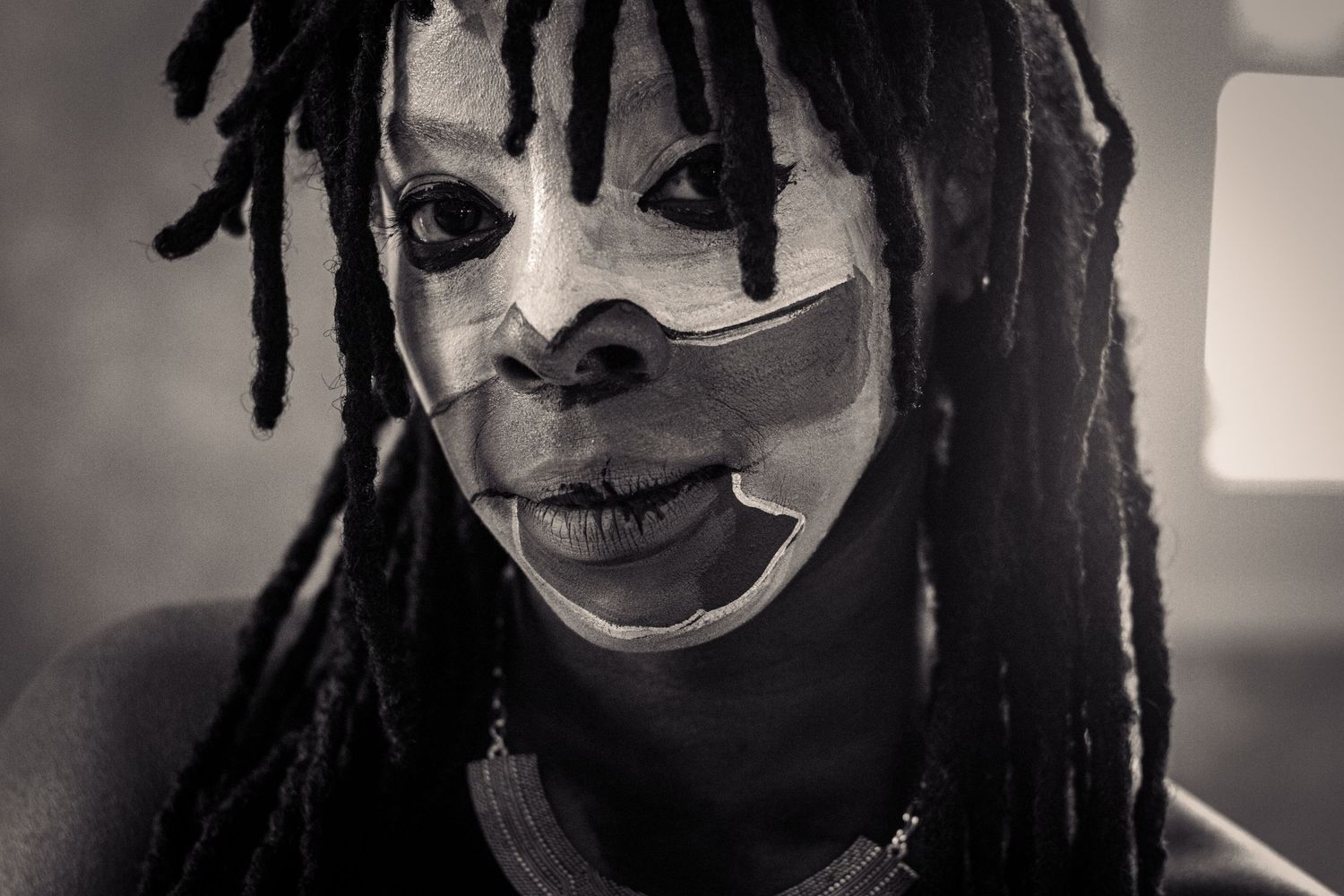 Black and white portrait of a person with dreadlocks wearing traditional face paint.