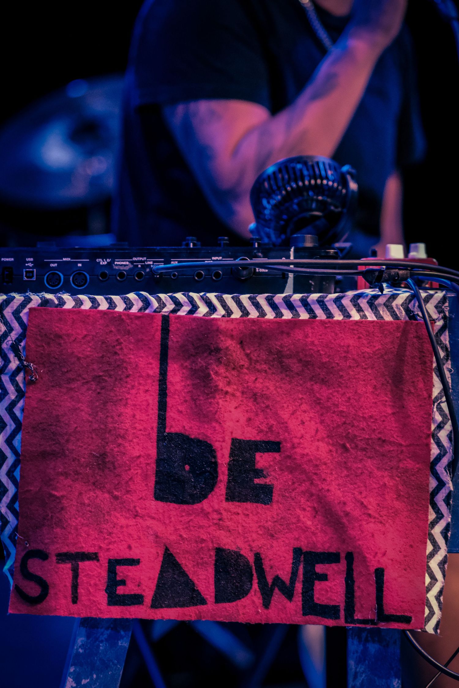 Close-up of a red sign reading Be Steadwell on a DJ table at a live music performance event.