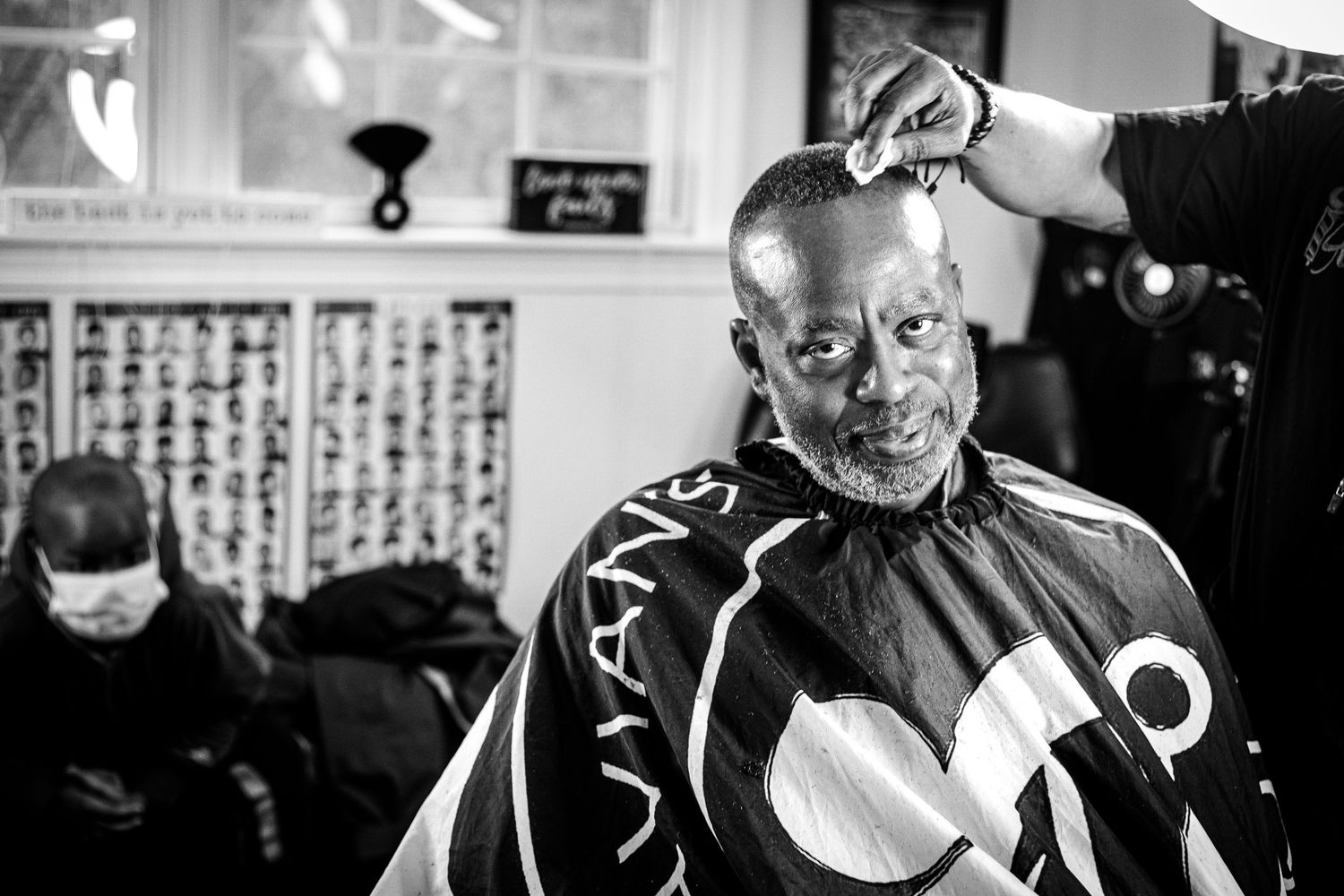 Black and white photo of a bald Black man getting a haircut in a vintage barbershop.