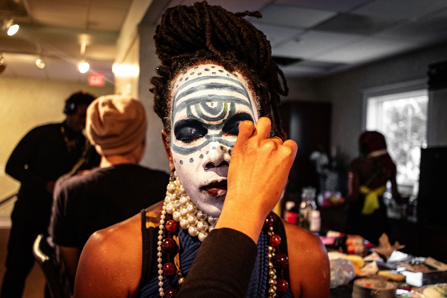 Artist applies intricate tribal face paint with geometric patterns on a performer wearing beaded necklaces.