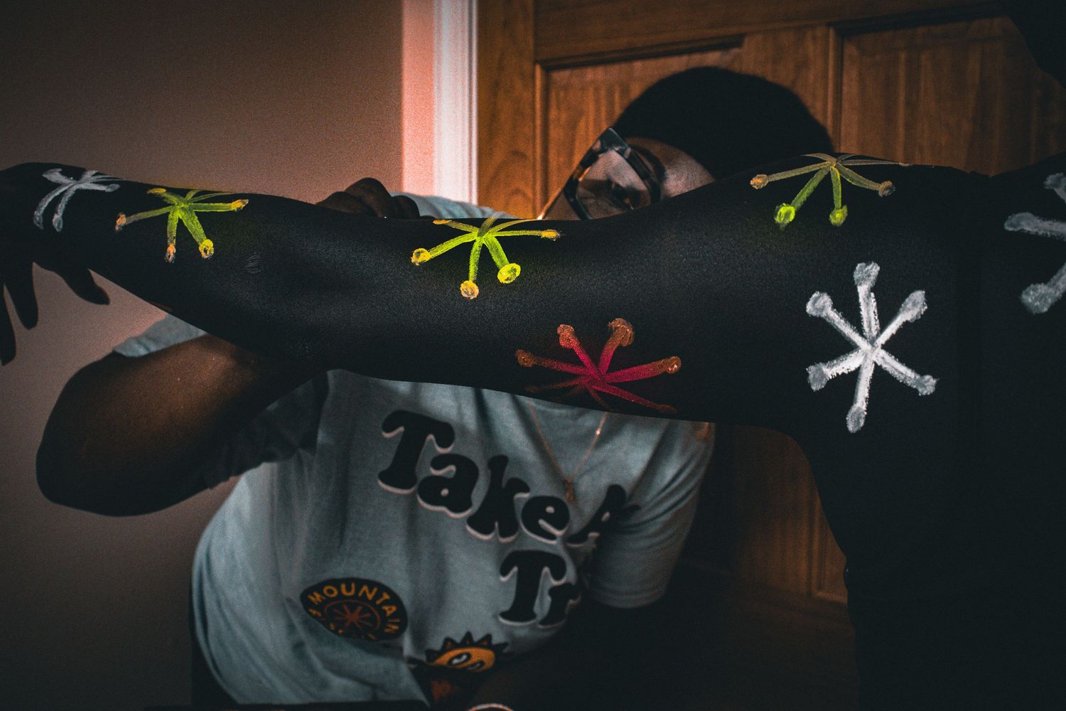 Person in a white graphic tee covering face with a decorated black sleeve with colorful designs.