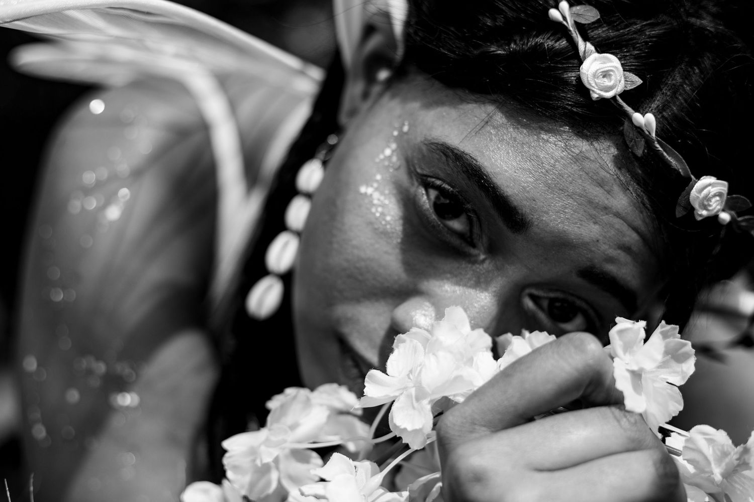 Close-up black and white portrait of a young woman with floral hair accessories holding white flowers near her face.