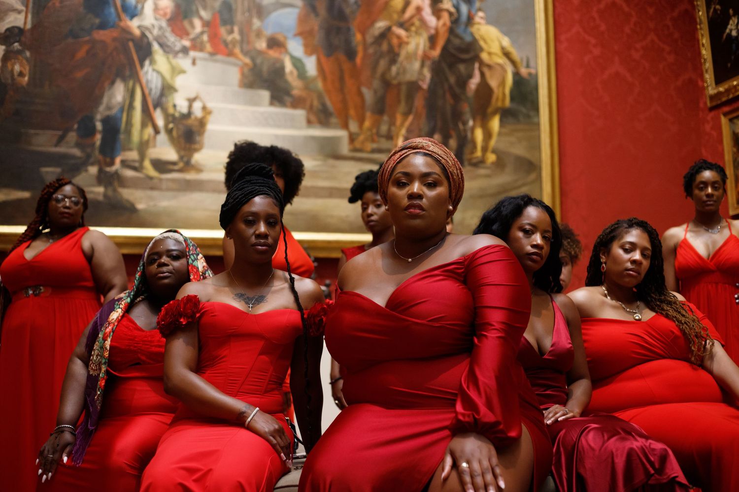 Group of Black women in red dresses posing before classical painting.